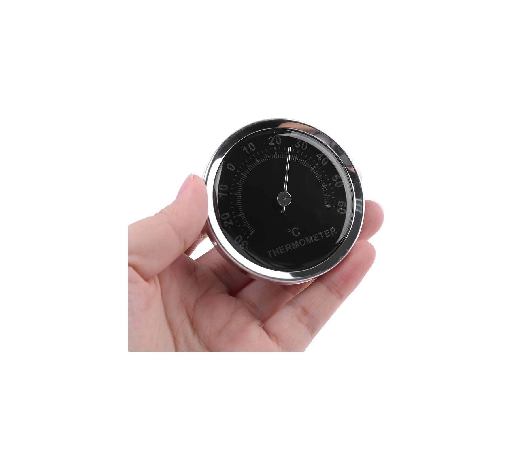 Eine Hand hält ein rundes, schwarzes Zifferblatt-Thermometer mit Celsius-Skala vor weißem Hintergrund.