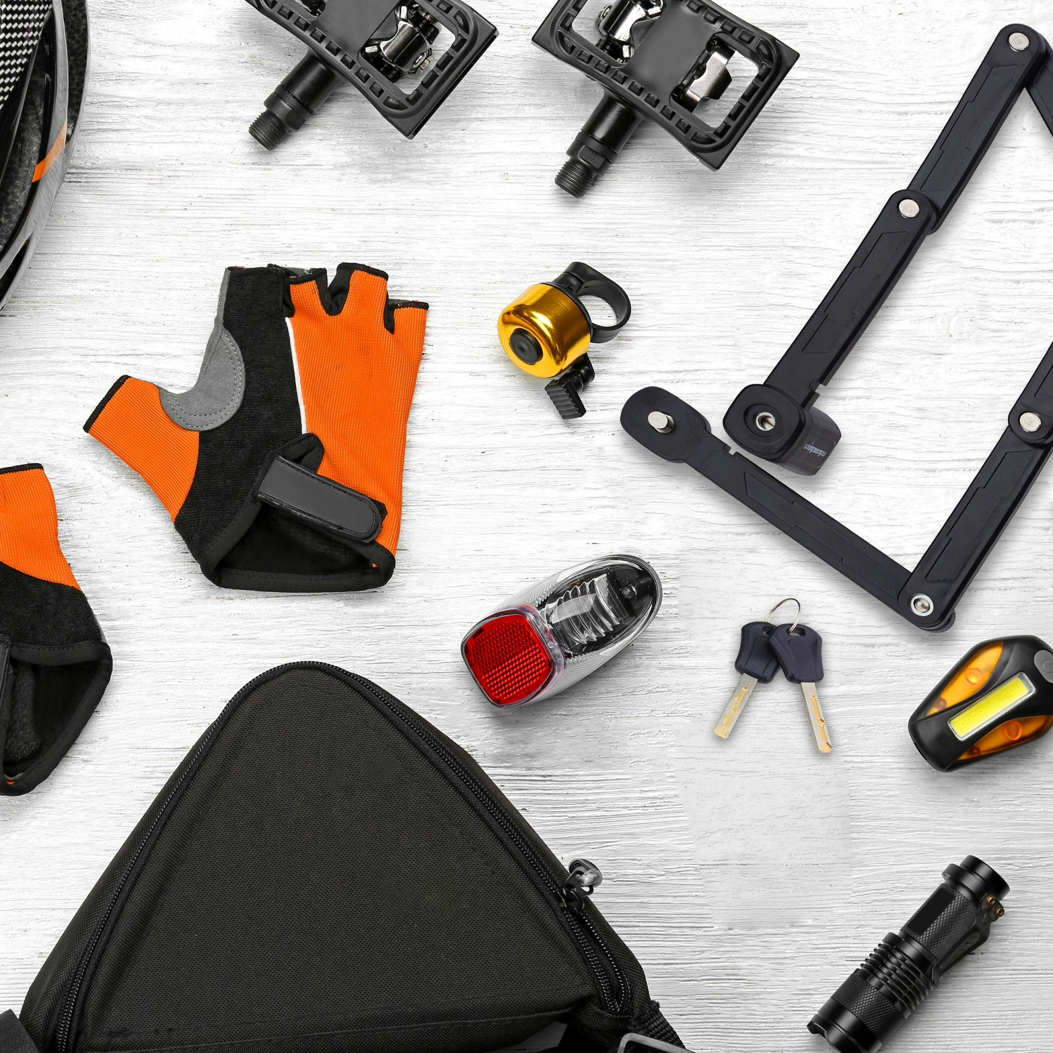 Fahrradzubehör wie Helm, Handschuhe, Schloss, Licht und Tasche auf weißem Holzhintergrund.