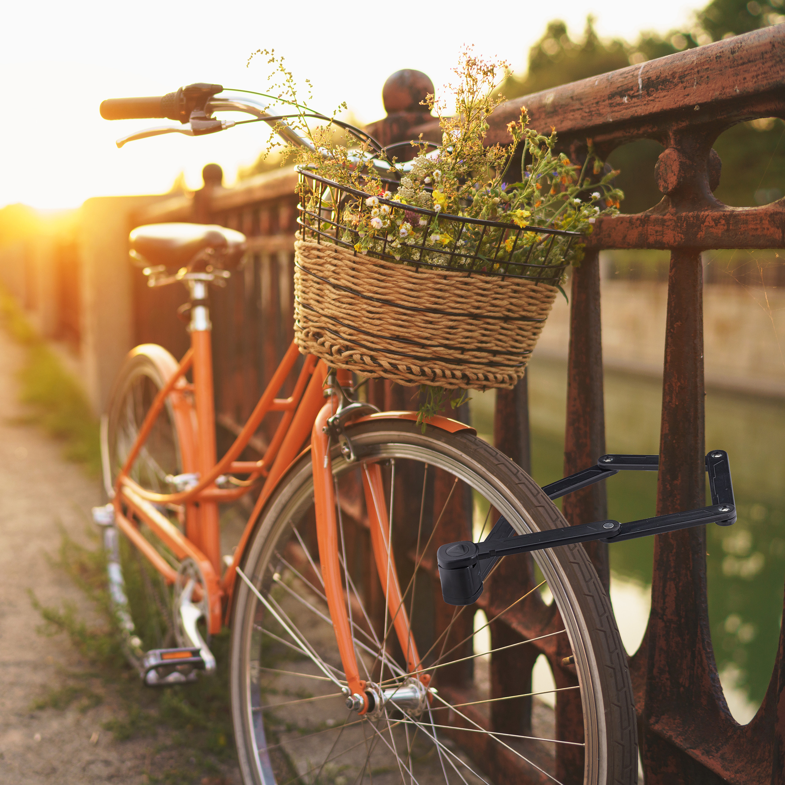 Ein orangefarbenes Fahrrad mit Blumenkorb steht bei Sonnenuntergang an einer Brücke mit Schloss.