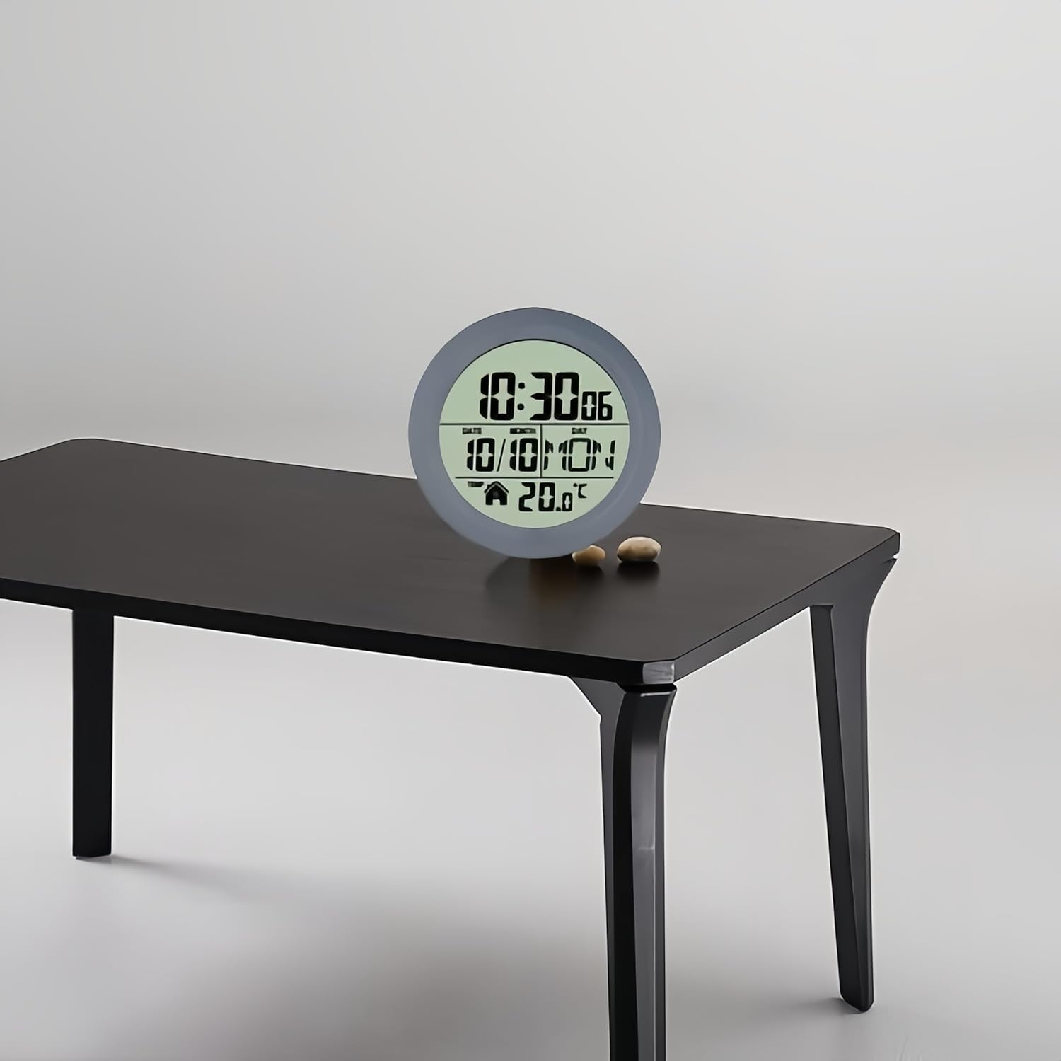 Eine graue digitale Wanduhr steht auf einem dunklen Holztisch vor weißem Hintergrund.