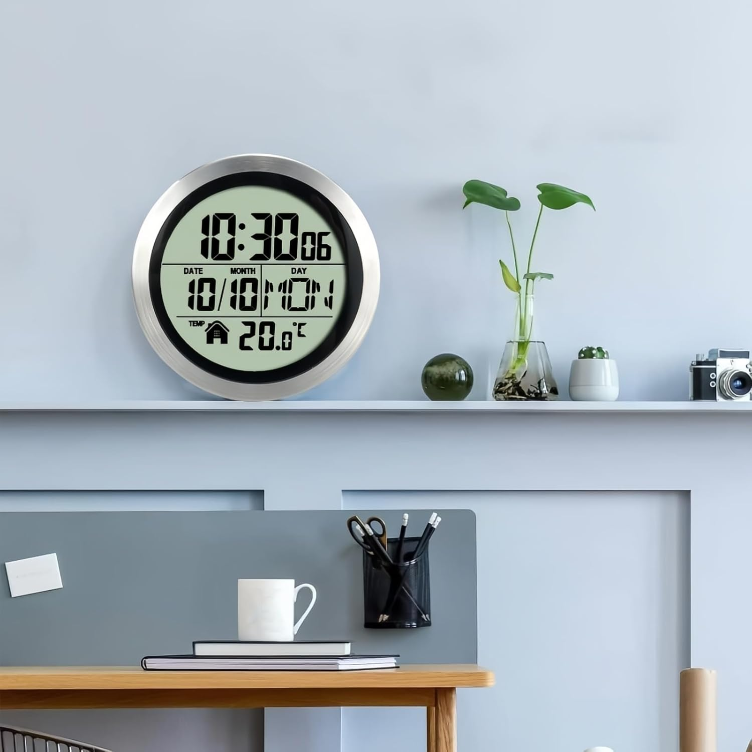 Eine runde digitale Wanduhr mit Silberrand hängt an einer blauen Wand über einem Regal mit Dekoration.