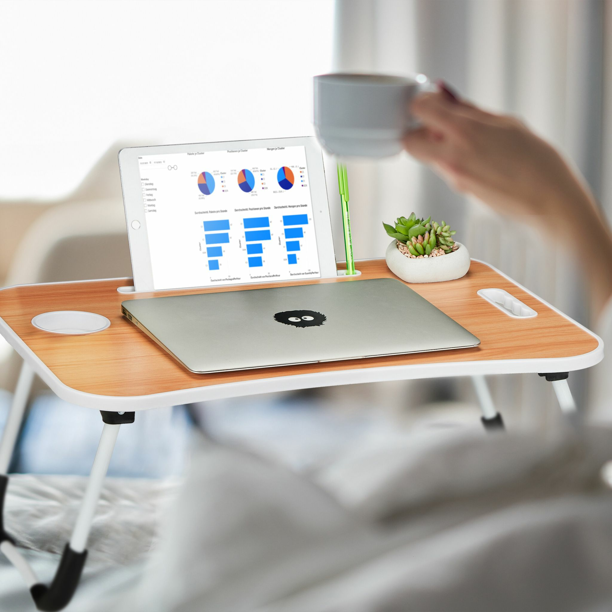 Ein Holztisch im Bett mit Laptop, Tablet, Stift, Sukkulente und einer Kaffeetasse.