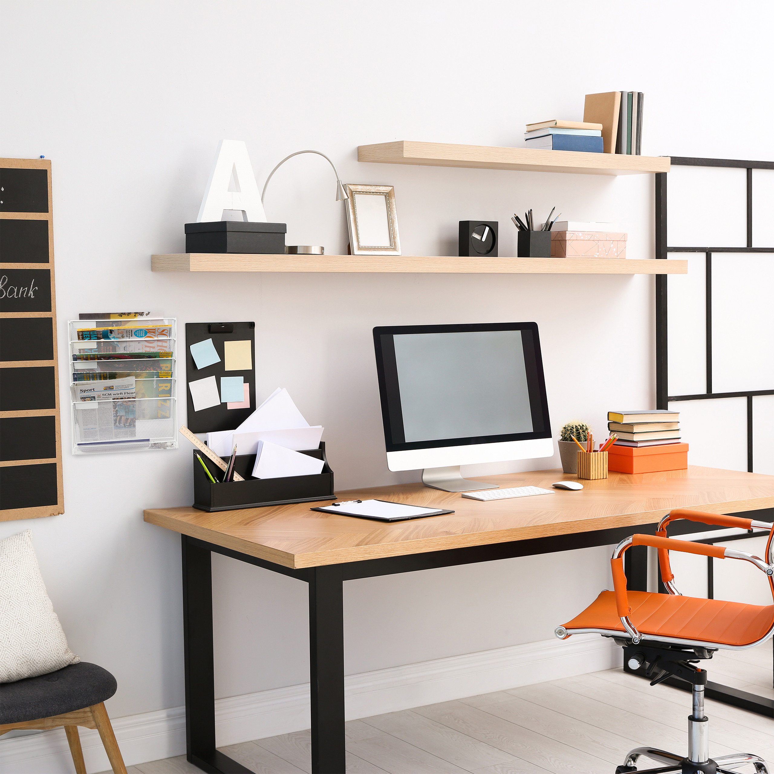 Moderne Arbeitsplatz mit Holztisch, Computer, Regalen und einem orangen Bürostuhl vor weißer Wand.