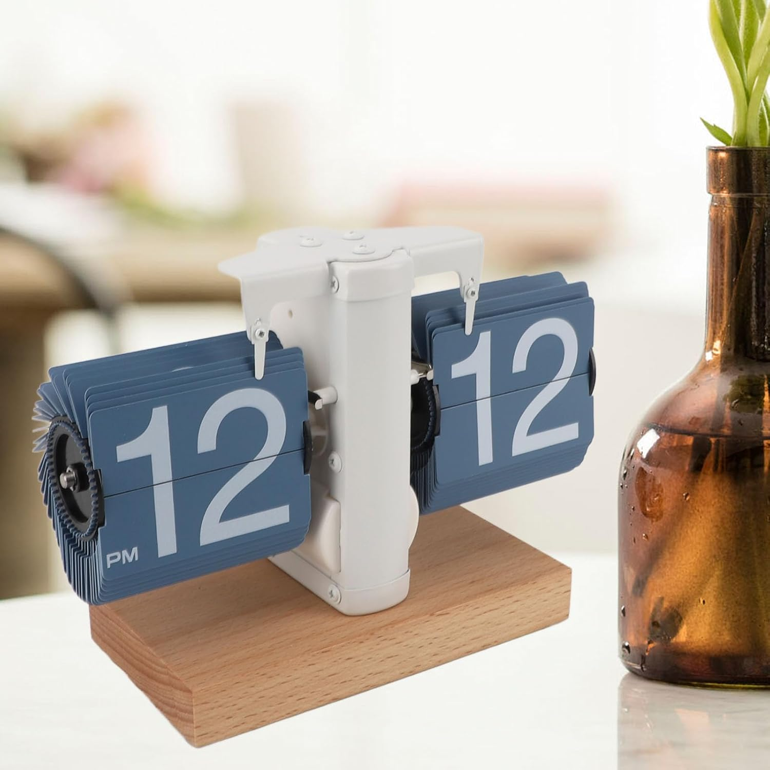 Eine weiß-blaue Flip-Uhr auf einem Holzsockel mit einer Glasflasche daneben.