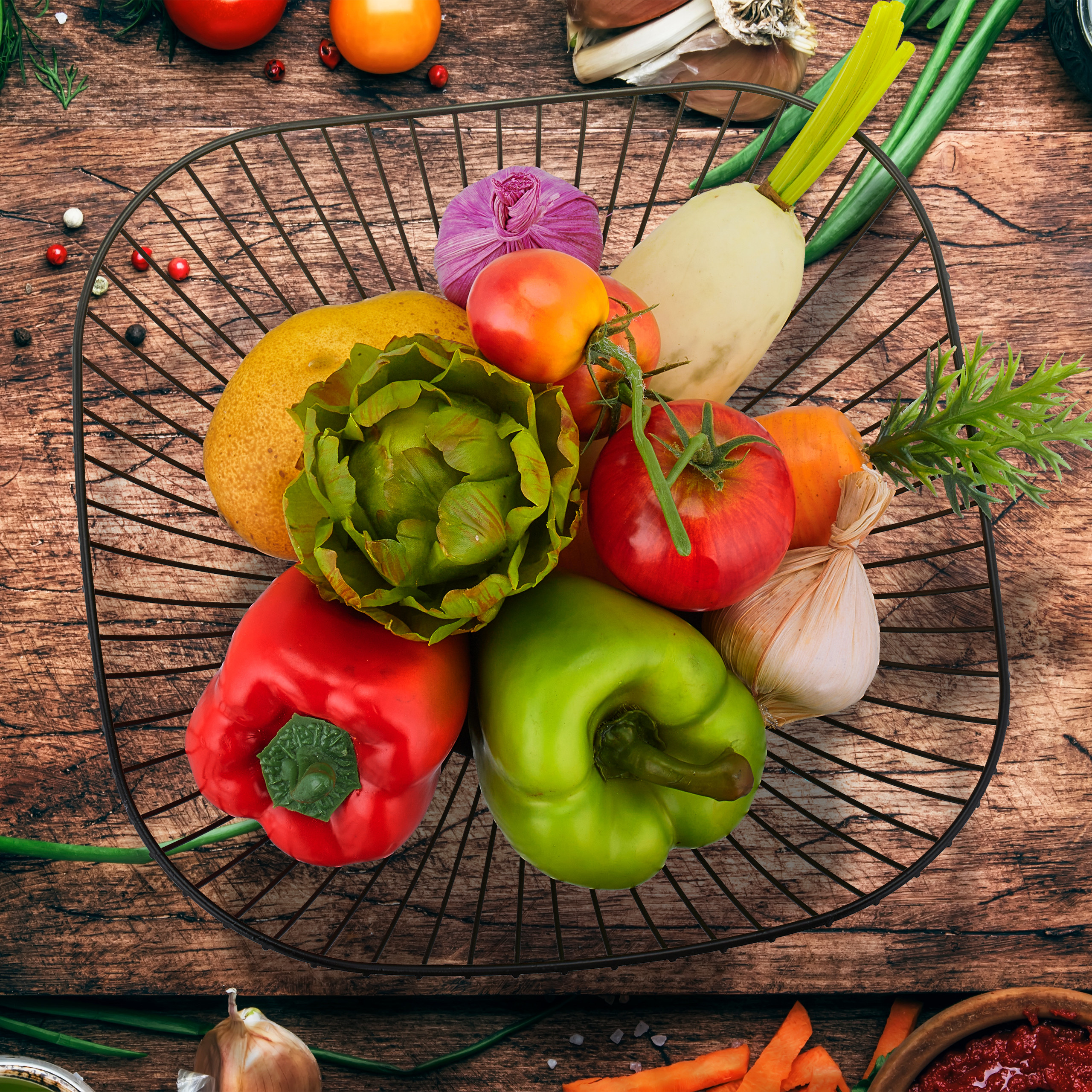 Un cestino di metallo con verdure fresche tra cui peperoni, pomodori e un carciofo su legno.