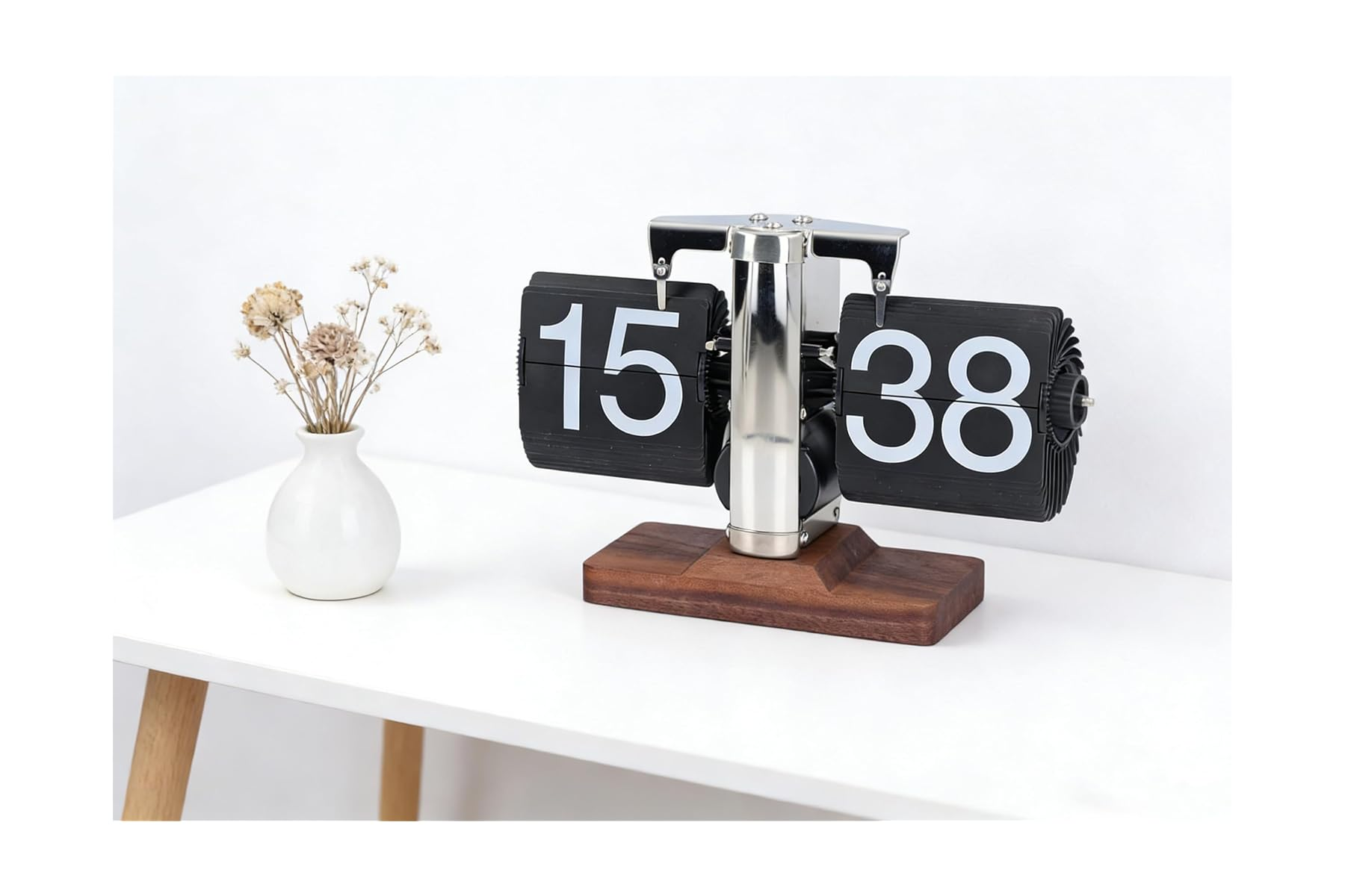 Eine Vintage-Flip-Uhr mit der Anzeige 15:38 steht auf einem Holzsockel neben einer kleinen weißen Vase mit Trockenblumen.