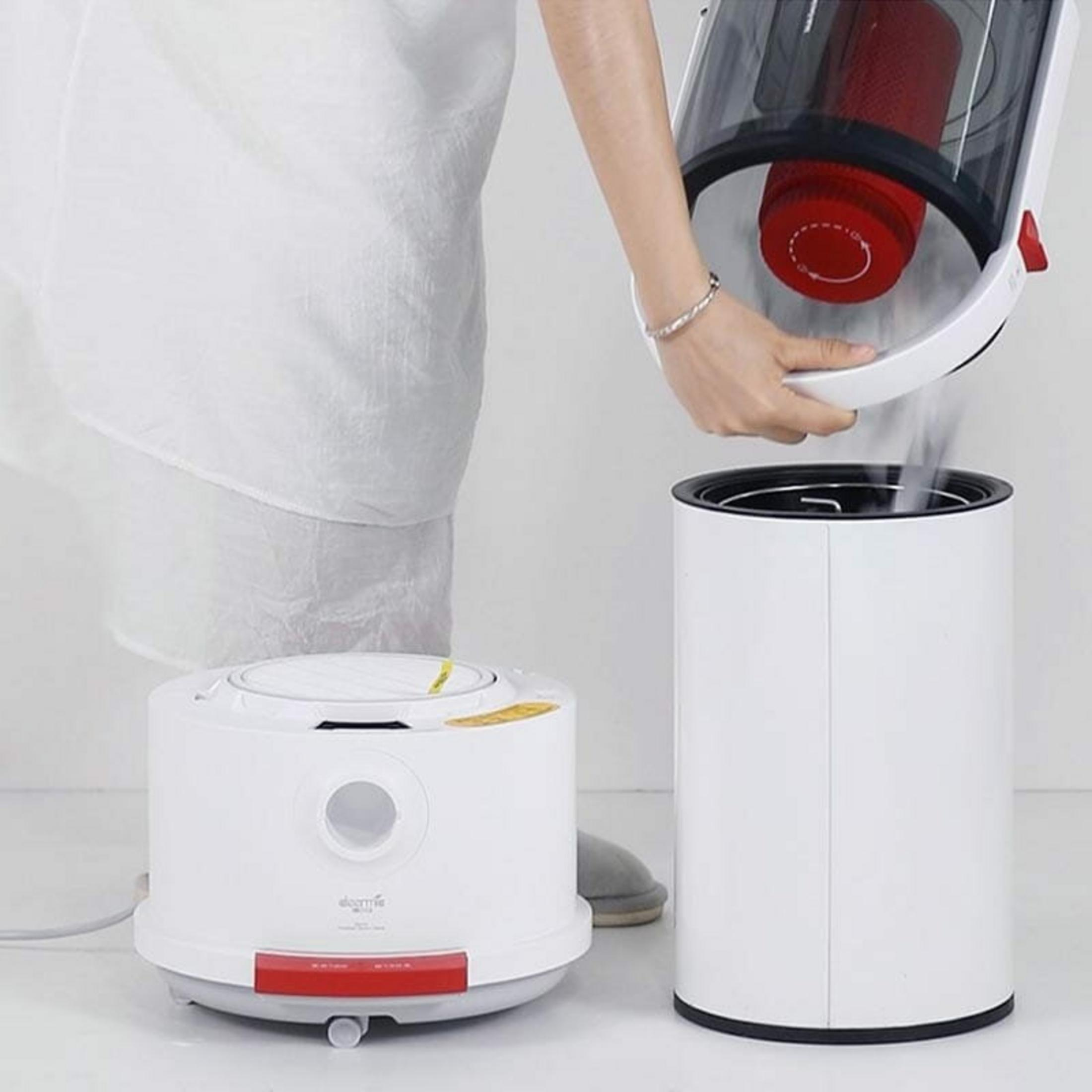Una persona svuota il contenitore della polvere rosso e bianco di un aspirapolvere.