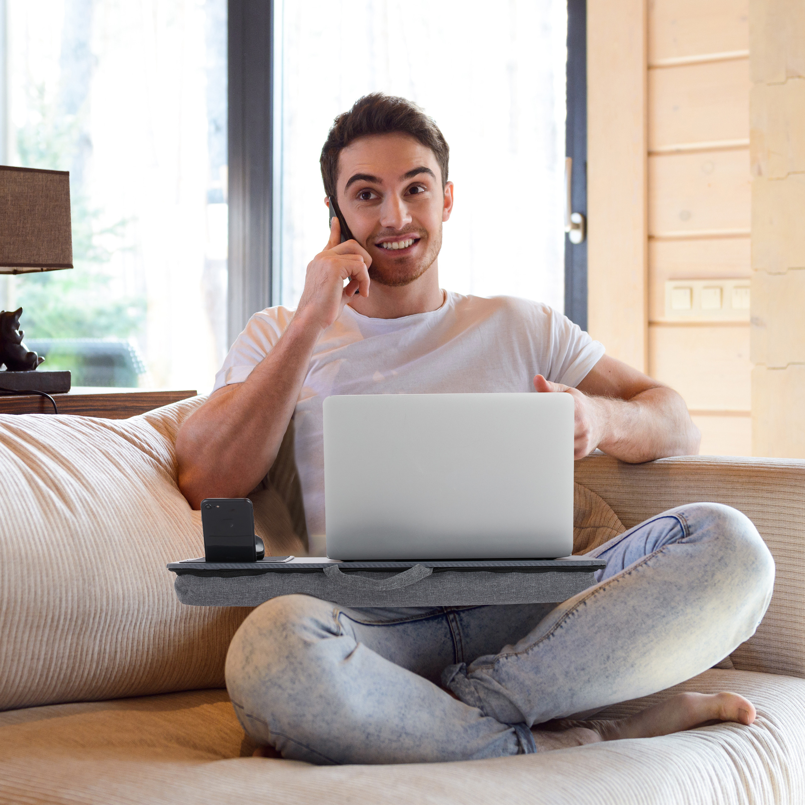 Ein lächelnder Mann sitzt auf einem Sofa, telefoniert und hält einen Laptop auf seinem Schoß.
