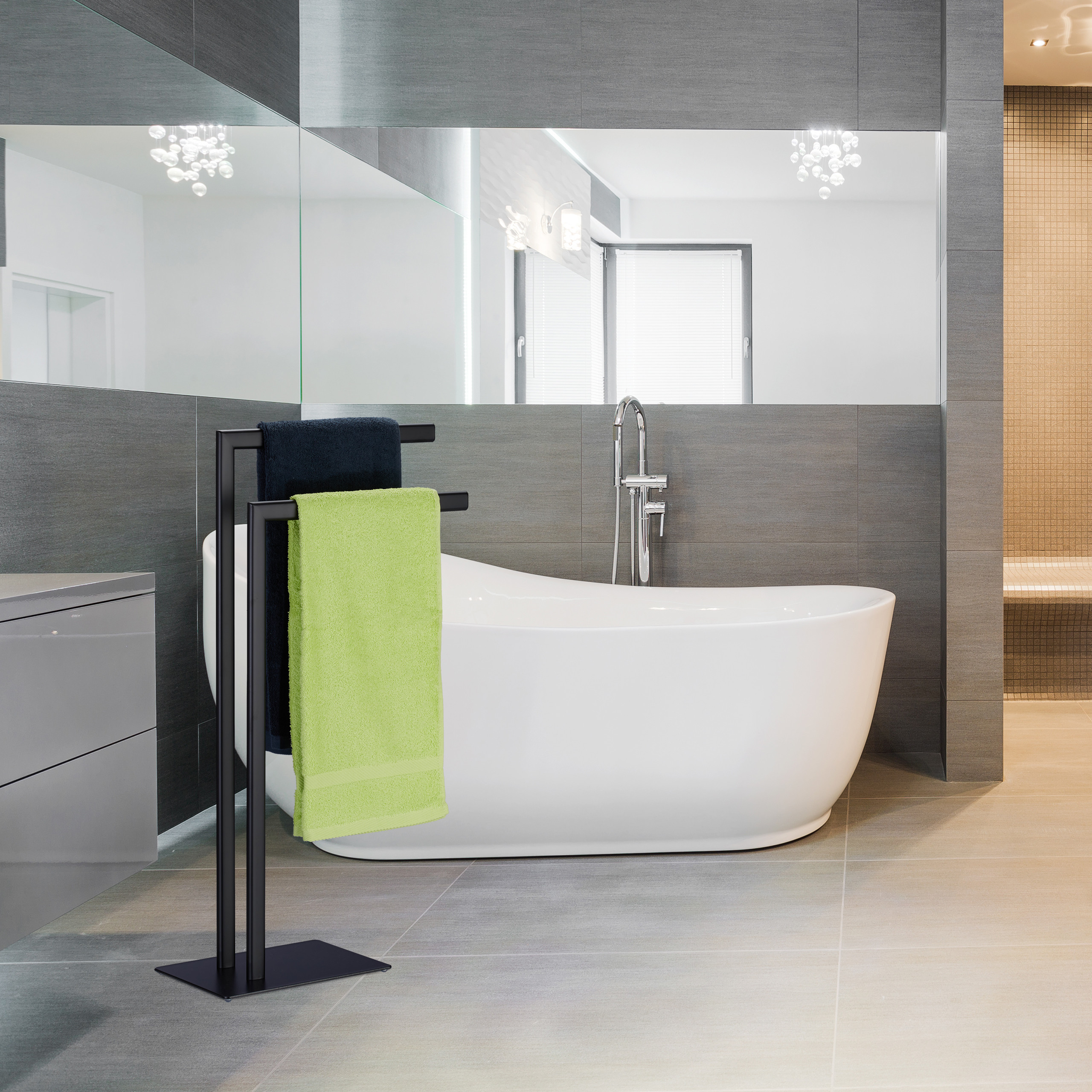 Moderne Badewanne mit schwarzem Handtuchhalter, auf dem grüne und blaue Handtücher hängen, vor grauen Fliesen.