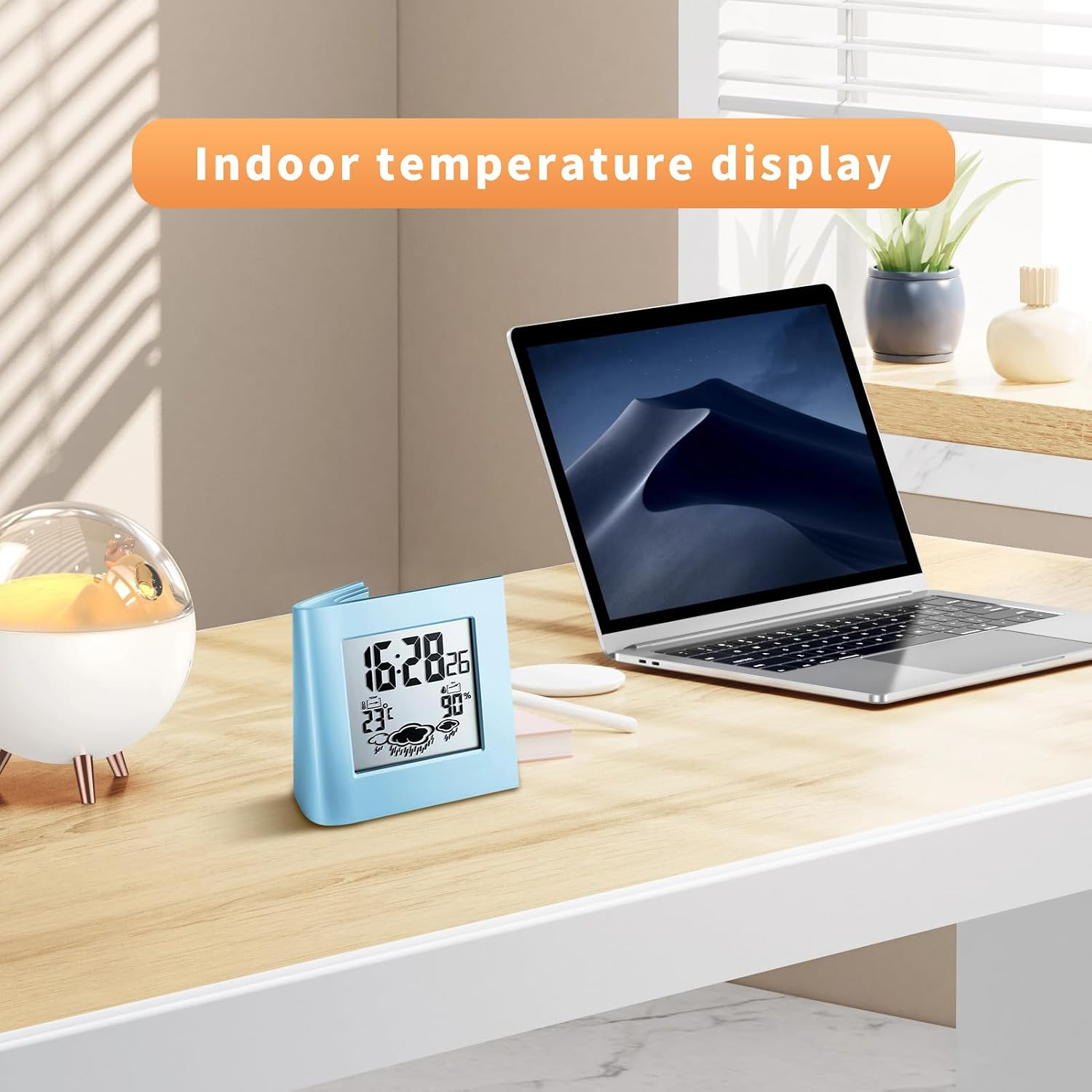 Blaue Digitaluhr mit Temperaturanzeige auf einem Holztisch neben einem Laptop.