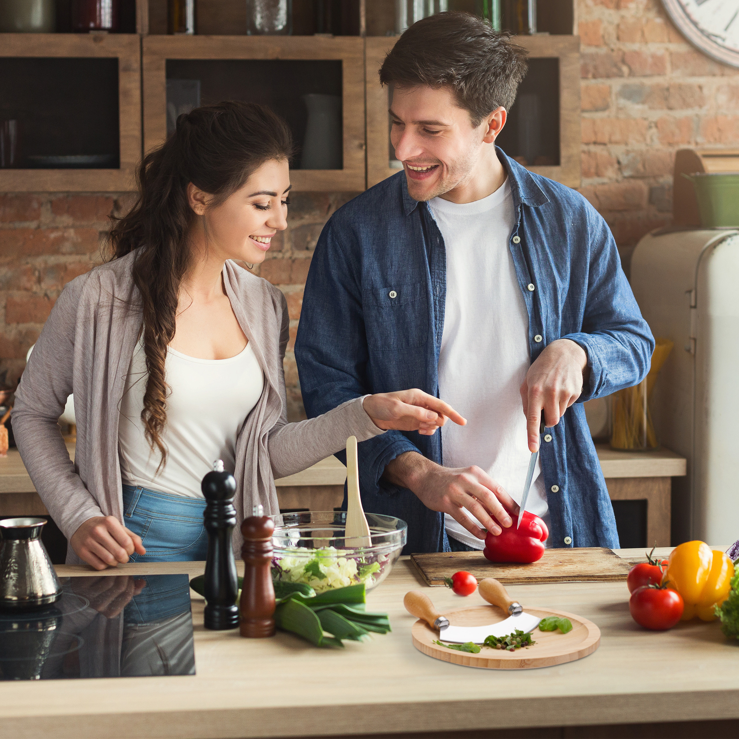 Ein junges Paar kocht zusammen in einer Küche, schneidet rote Paprika neben einer Salatschüssel und Gemüse.
