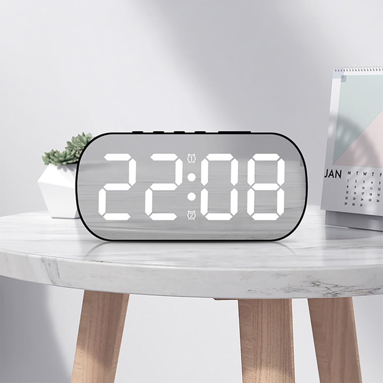 Digitale LED-Uhr mit spiegelnder Oberfläche und weißer Zeitangabe 22:08 auf einem Tisch mit Pflanze und Kalender.
