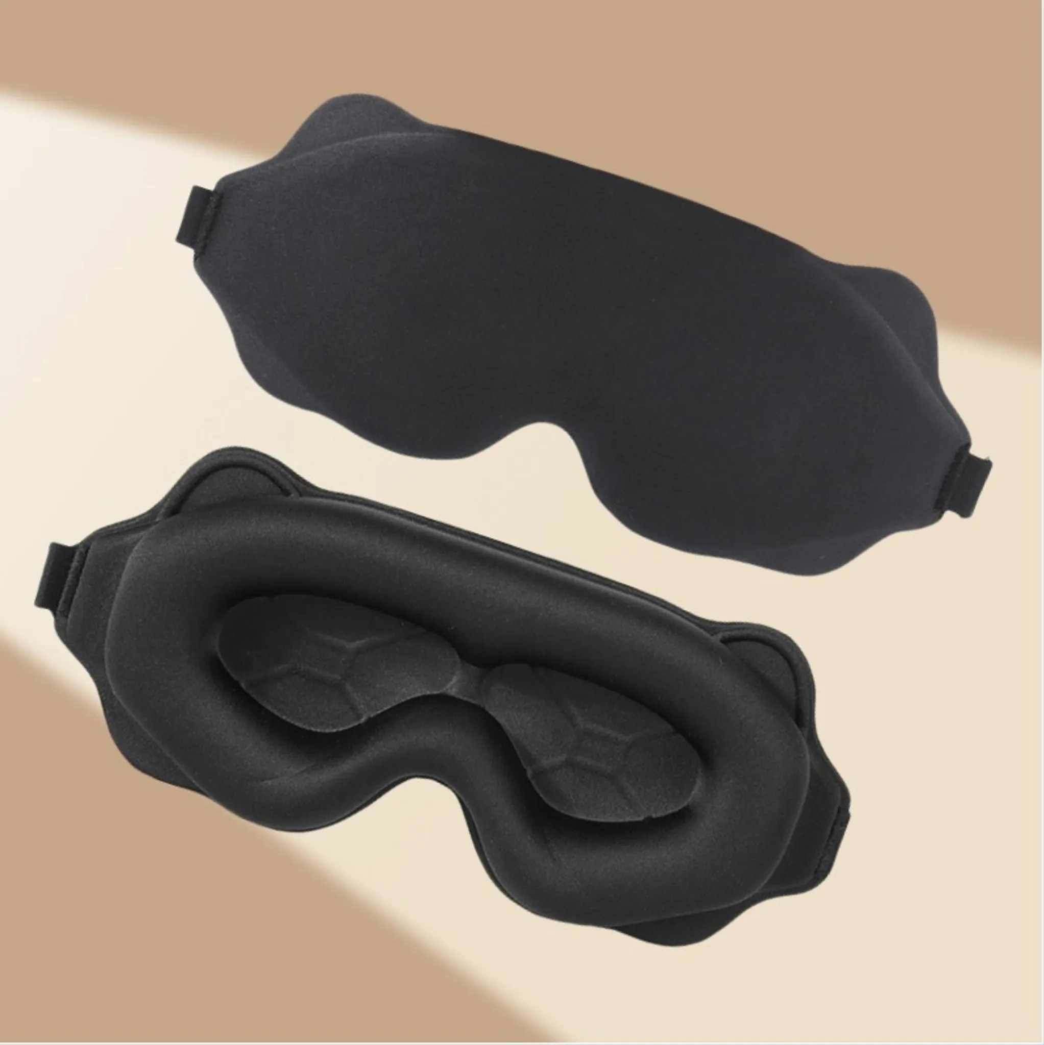 Zwei schwarze, konturierte Schlafmasken von vorne und hinten vor einem neutralen beige Hintergrund.