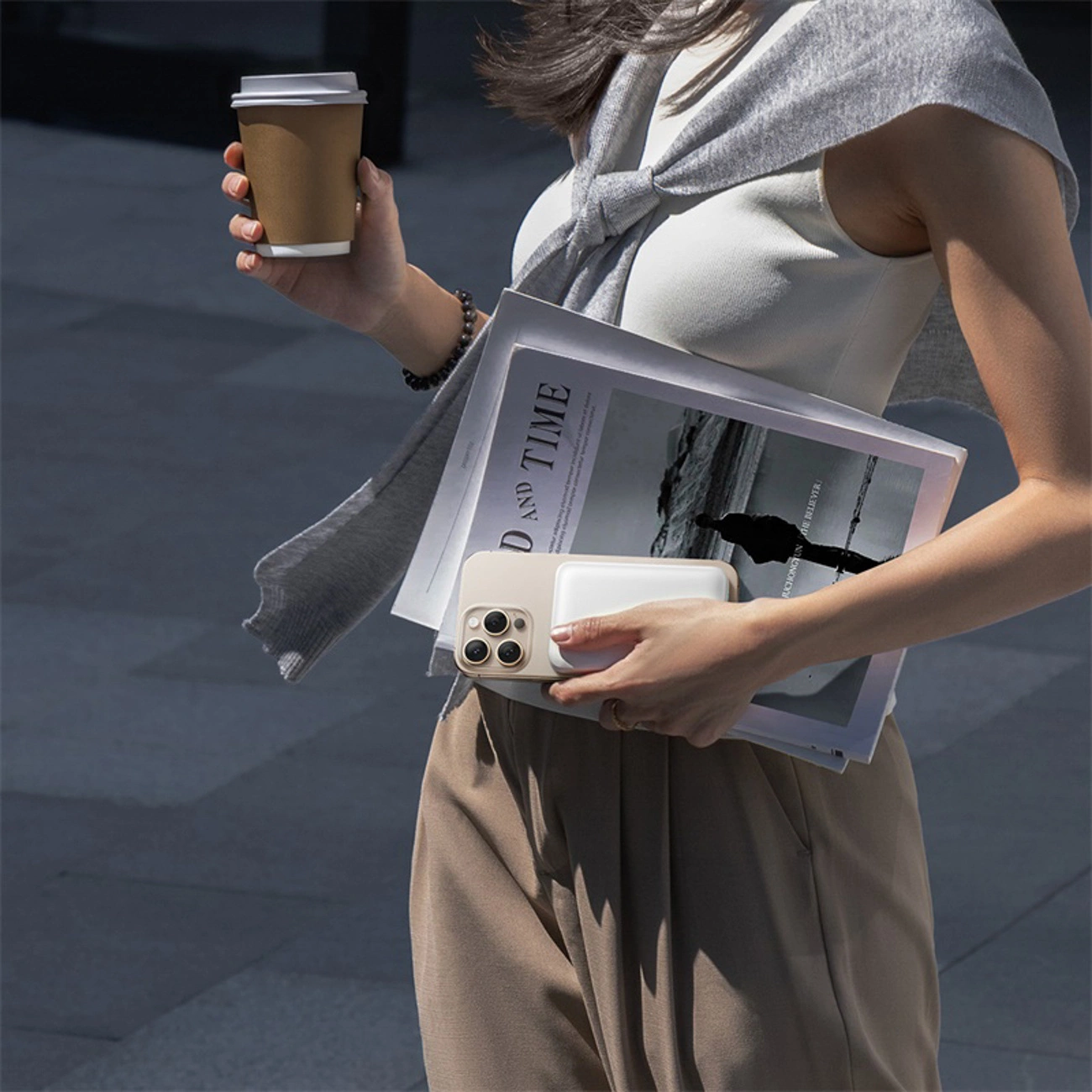 Una donna tiene in mano una tazza di caffè, riviste e uno smartphone con power bank.