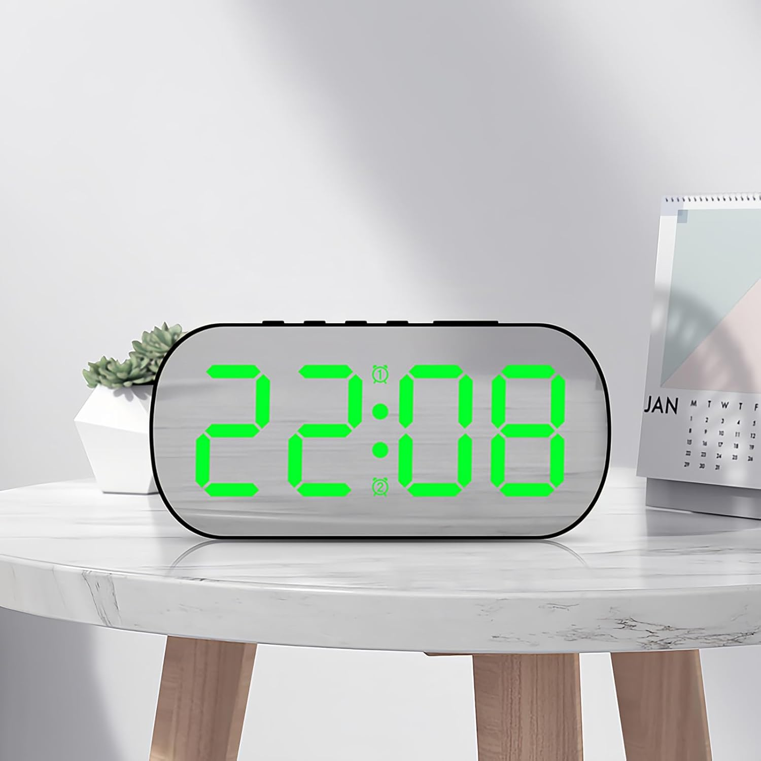 Digitale Weckuhr mit leuchtend grünen Zahlen auf einem weißen Marmortisch neben einem Kalender.