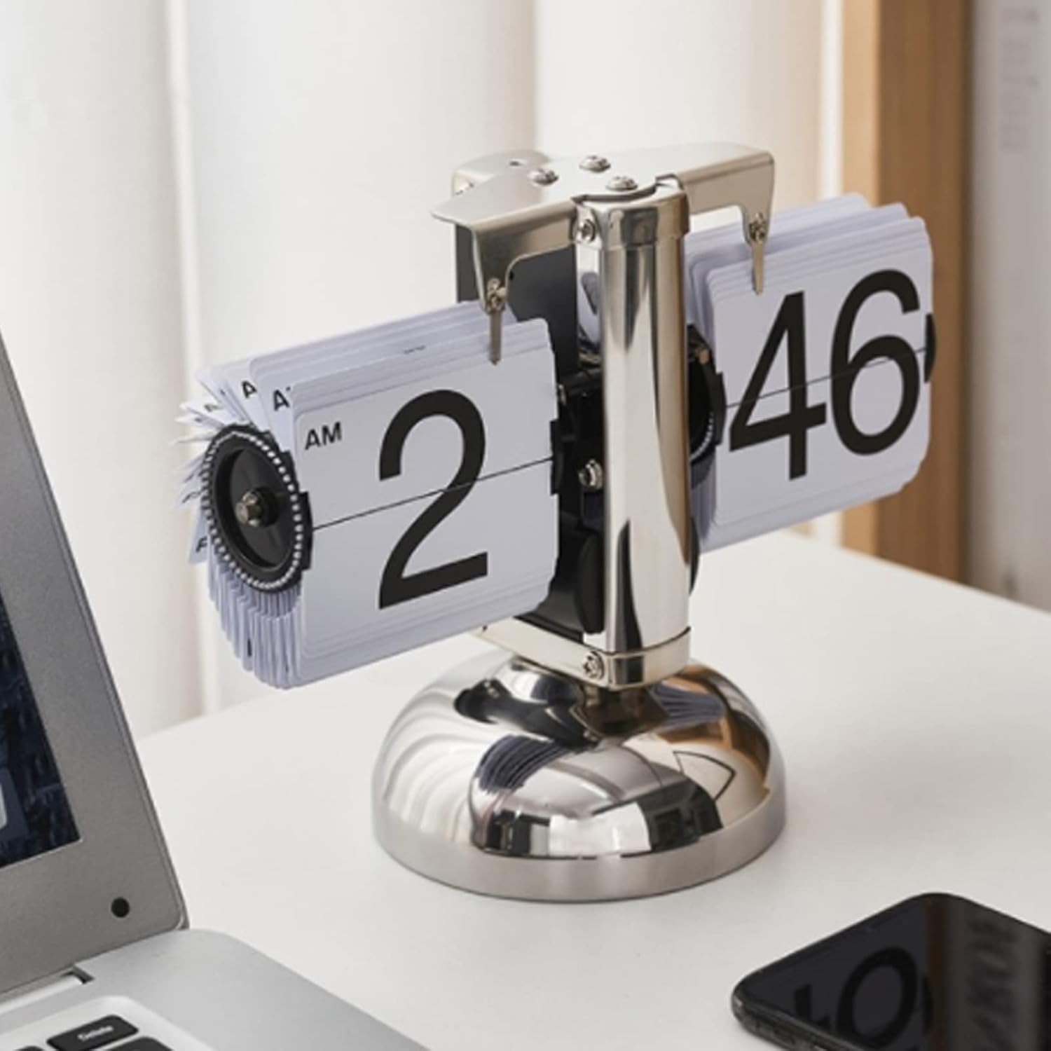 Eine silberne KlappzahlenUhr auf einem weißen Schreibtisch zeigt 2:46 neben einem Laptop und Smartphone.