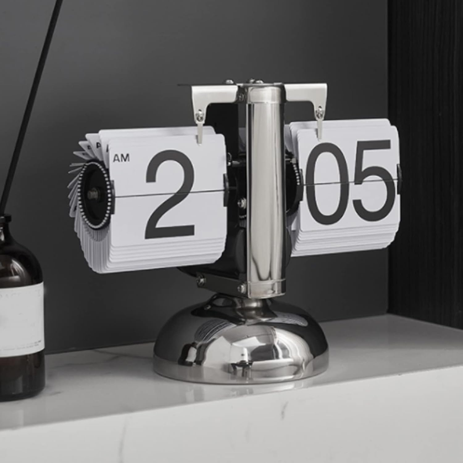 Eine silberne Retro-Flipuhr zeigt 02:05 AM auf einem weißen Tisch.