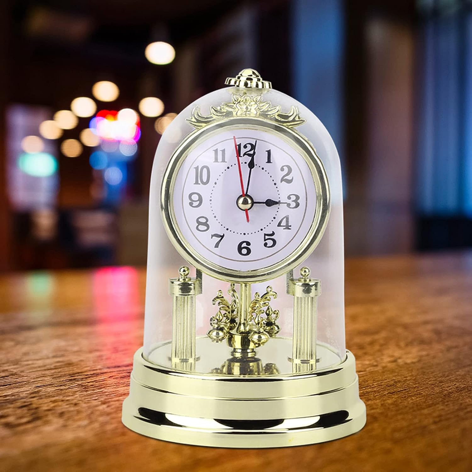 Eine goldgerahmte Uhr unter einer Glaskuppel steht auf einem Holztisch vor verschwommenem Hintergrund.