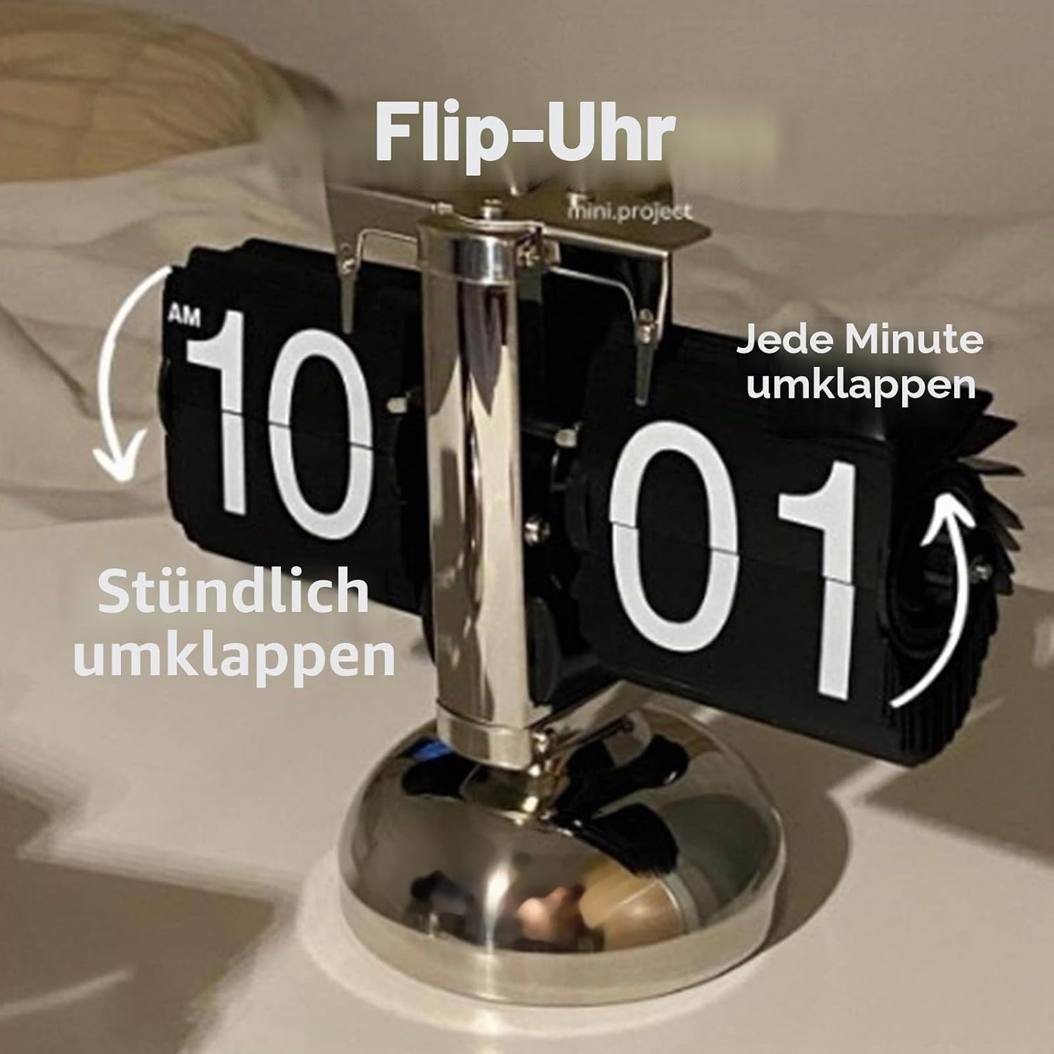 Eine silberne Flip-Uhr zeigt 10:01 mit deutschen Texten zum Klappmechanismus.