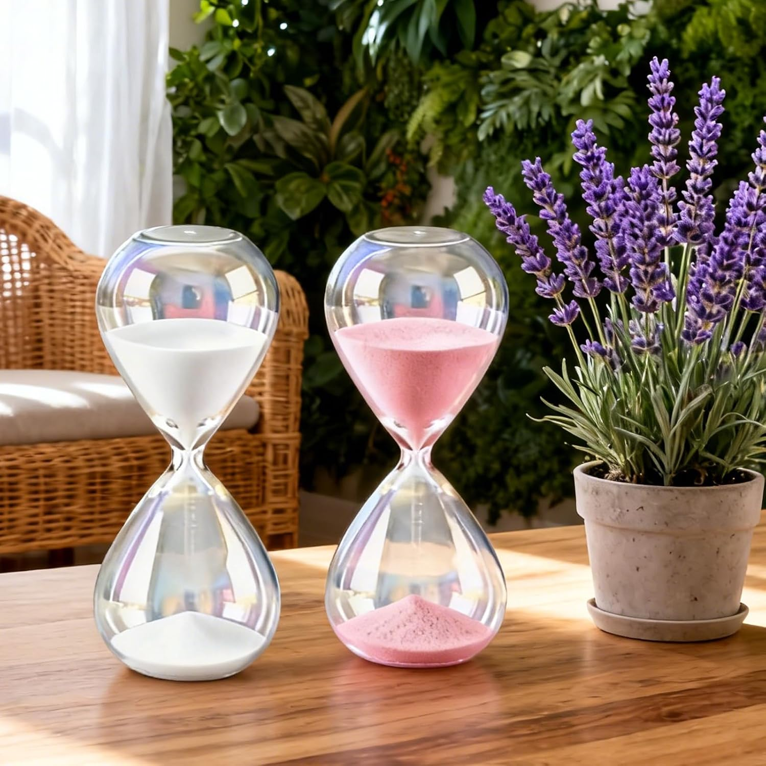 Zwei Sanduhren mit weißem und rosa Sand stehen auf einem Holztisch neben Lavendel.