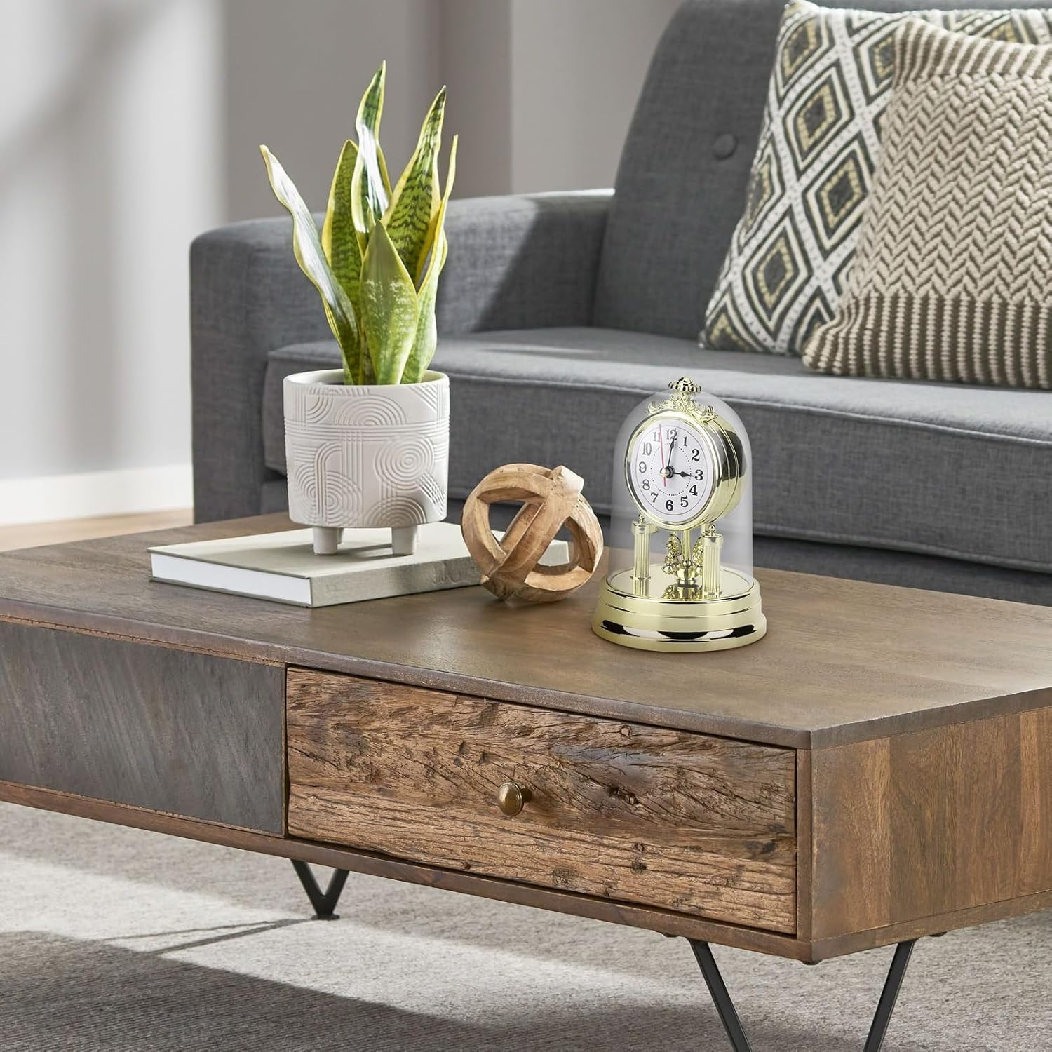 Holz-Couchtisch mit einer Topfpflanze, einer Holzkugel und einer kleinen Uhr unter einer Glasglocke, davor ein Sofa.