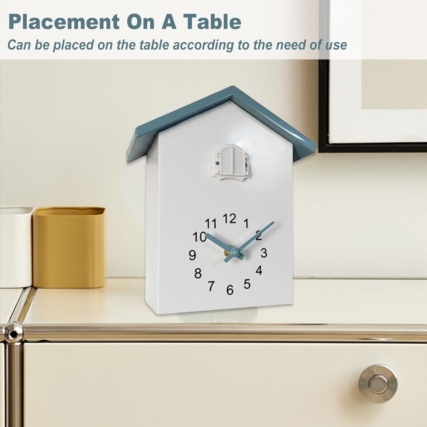 Eine weiße Uhr in Hausform mit blauem Dach steht auf einem Tisch vor einer Wand.