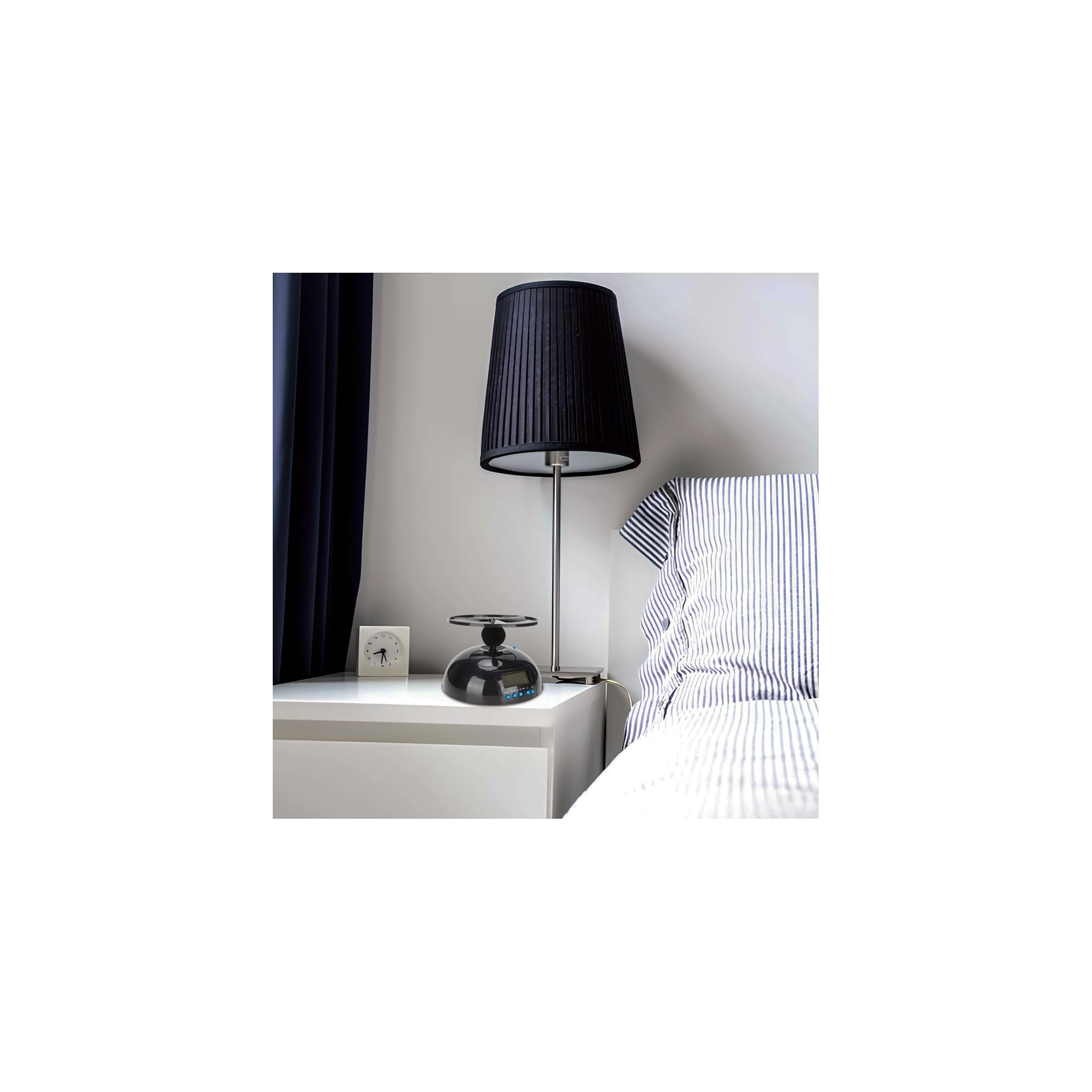 Nachttisch mit schwarzer Lampe, Uhr, Gadget neben blau-weiß gestreiftem Bett.