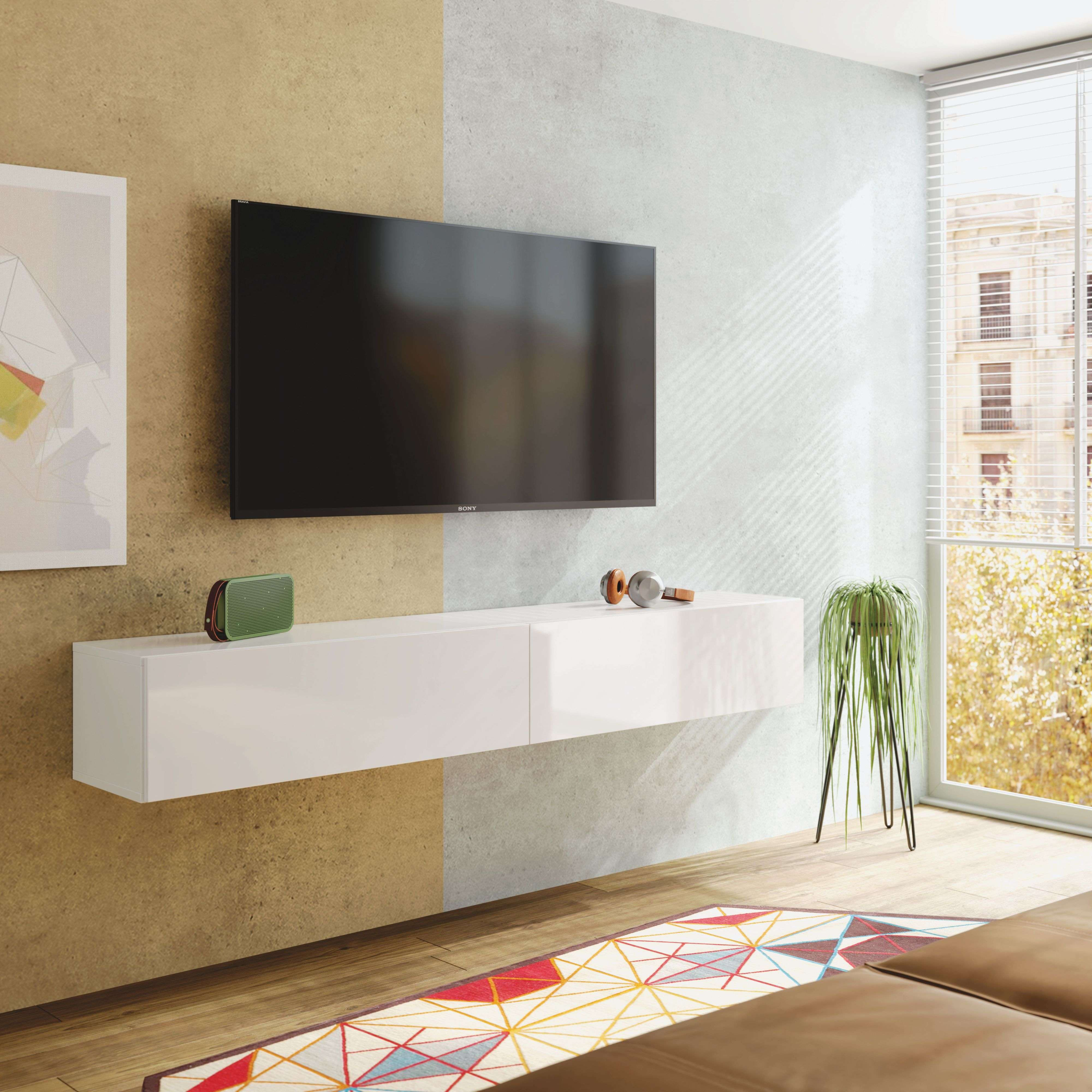 Un televisor negro en la pared sobre un mueble blanco, con un altavoz, auriculares y una planta.