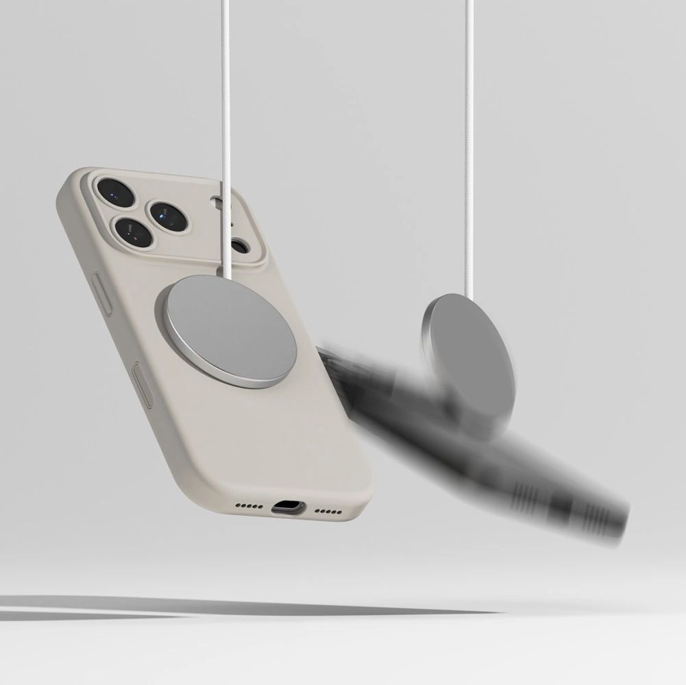Ein beiges Smartphone hängt an einem runden magnetischen Lade-Pad, während ein anderes verschwommen fällt.