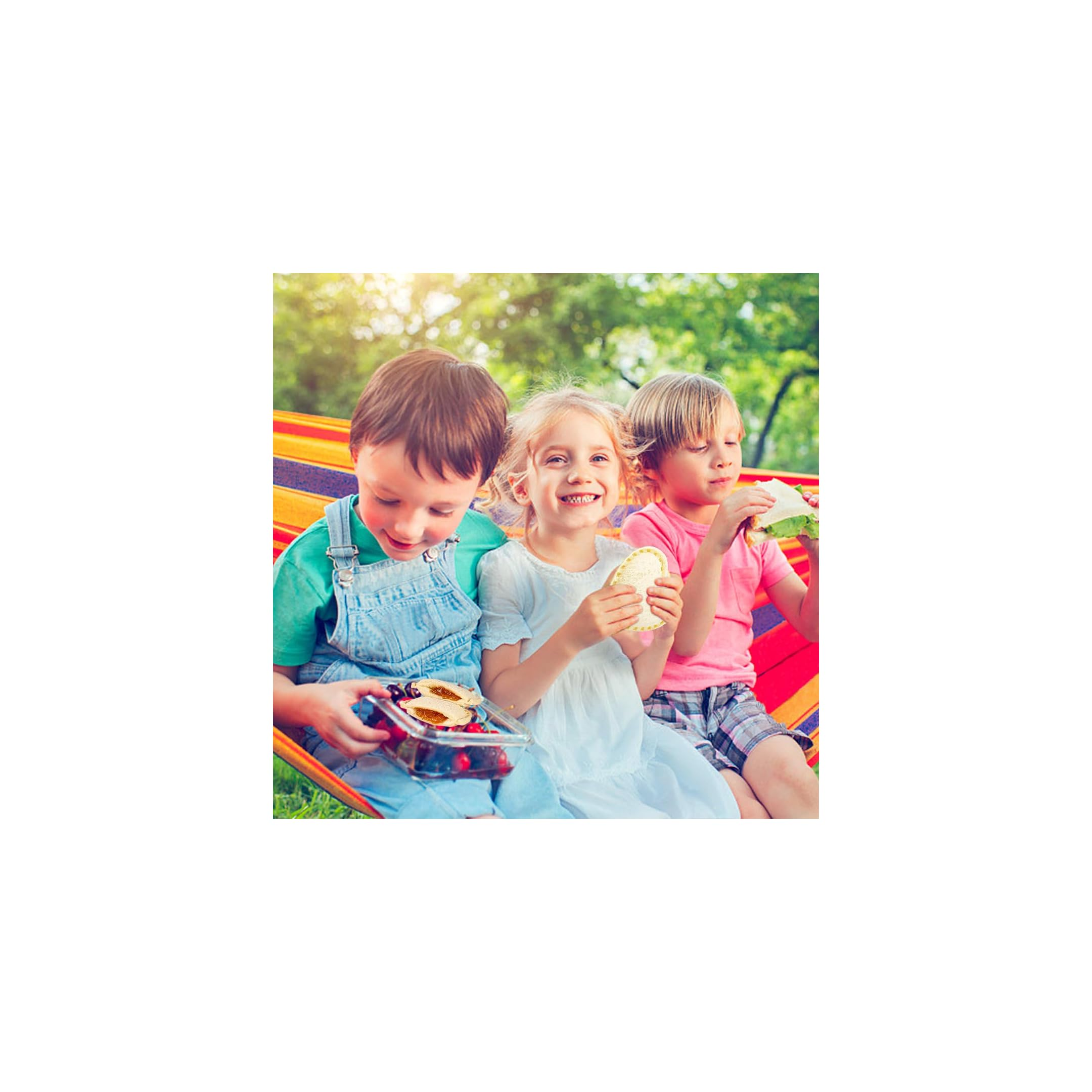 Drei Kinder sitzen in einer farbigen Hängematte und essen Sandwiches und Beeren im Freien.