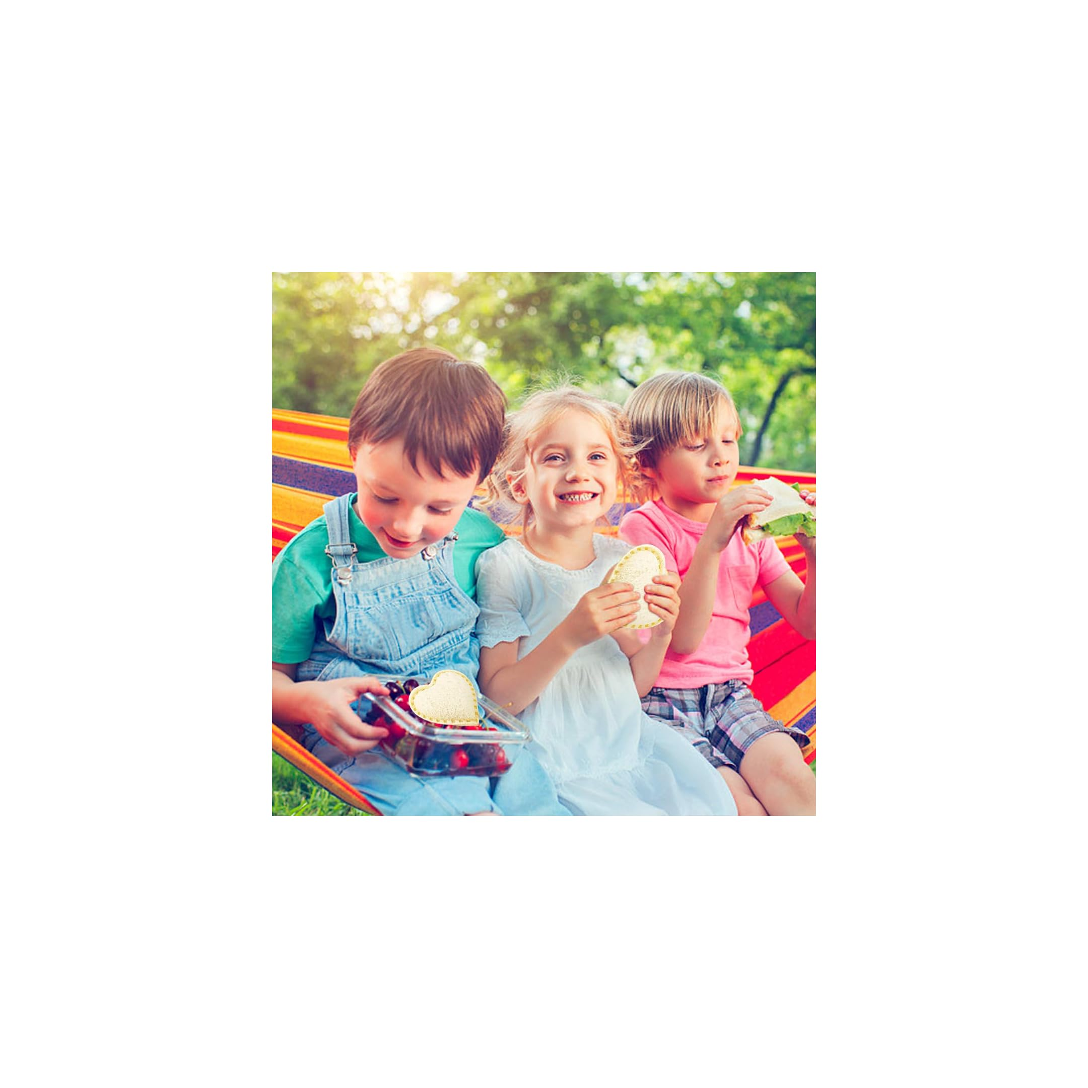 Drei Kinder sitzen in einer bunten Hängematte im Garten und essen Sandwiches und Beeren.