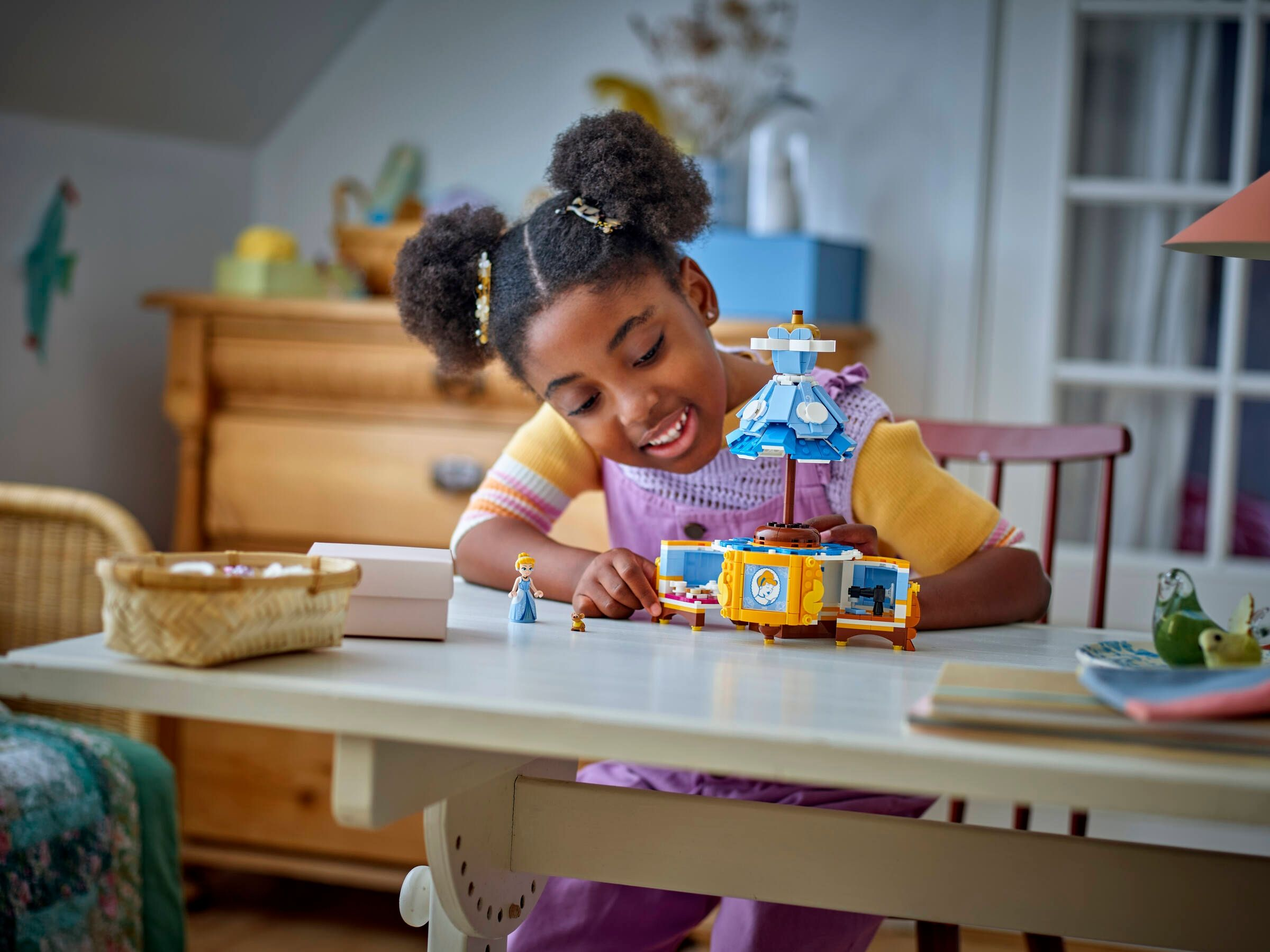 Ein junges Mädchen mit Pigtails baut an einem Holztisch ein Lego-Schloss auf.