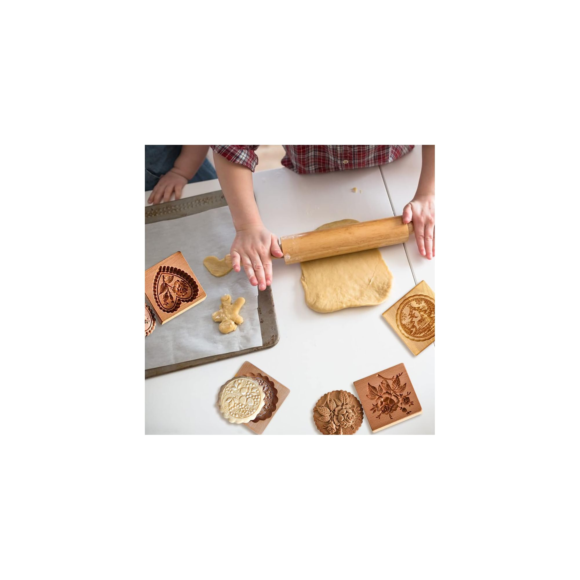 Kind rollt Teig aus, umgeben von Holzkeksformen auf weißem Tisch.