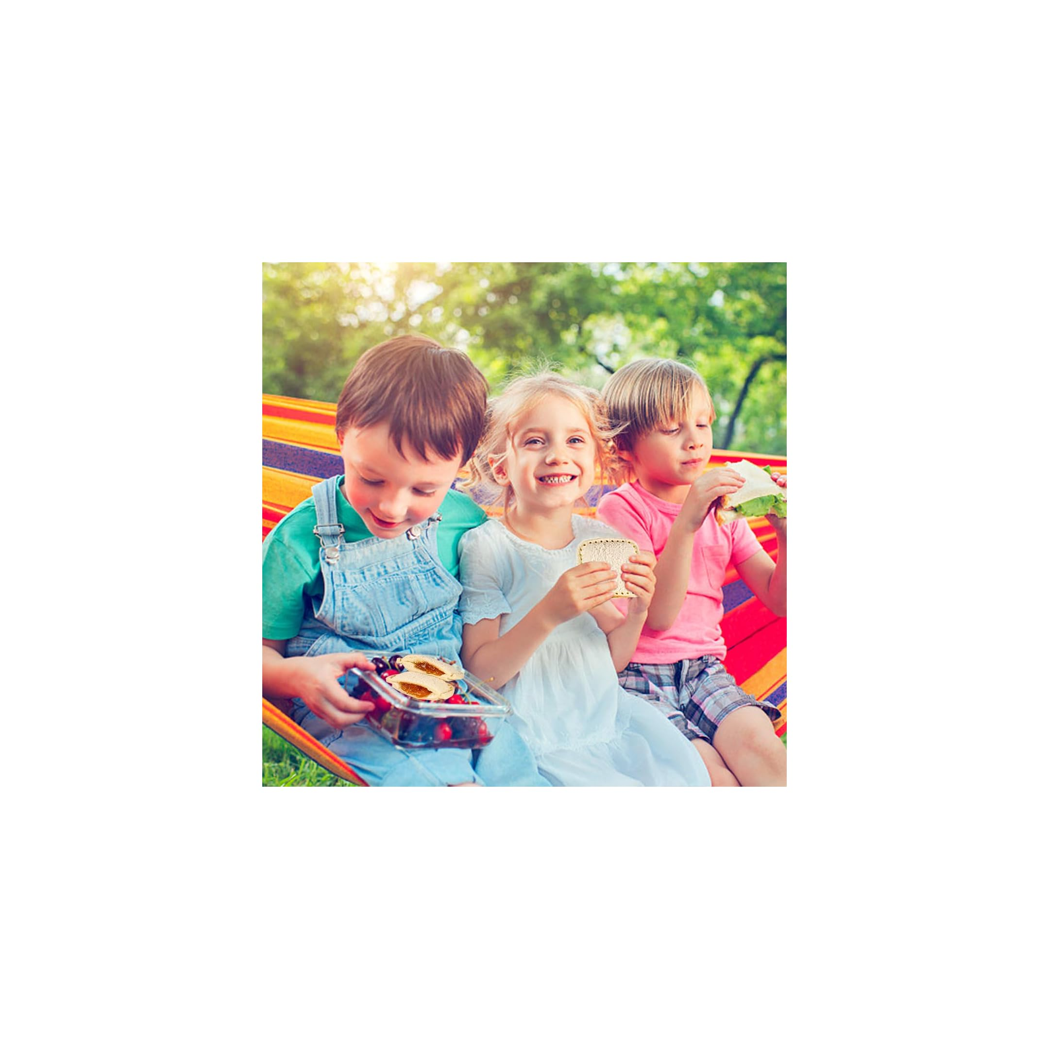 Drei fröhliche Kinder sitzen in einer Hängematte und essen Sandwiches und Beeren im Freien.