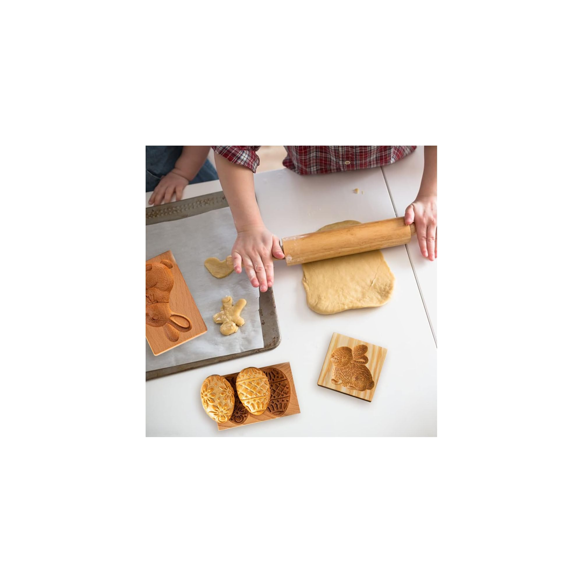 Personen rollen Teig auf einem weißen Tisch aus, umgeben von Holzbackformen und einem Backblech.