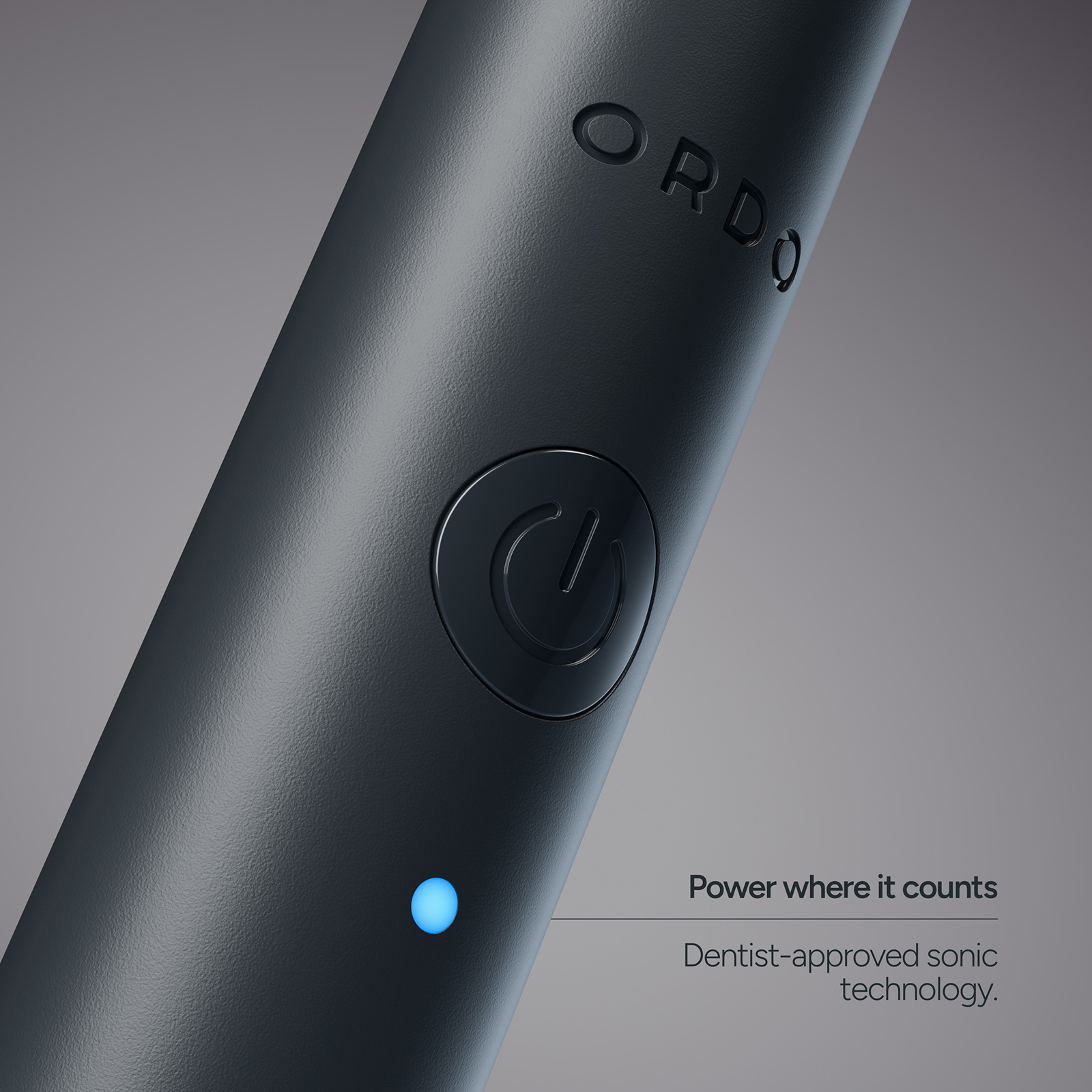 Primer plano de un cepillo de dientes eléctrico oscuro con el logotipo ORDO, botón de encendido y luz LED azul.
