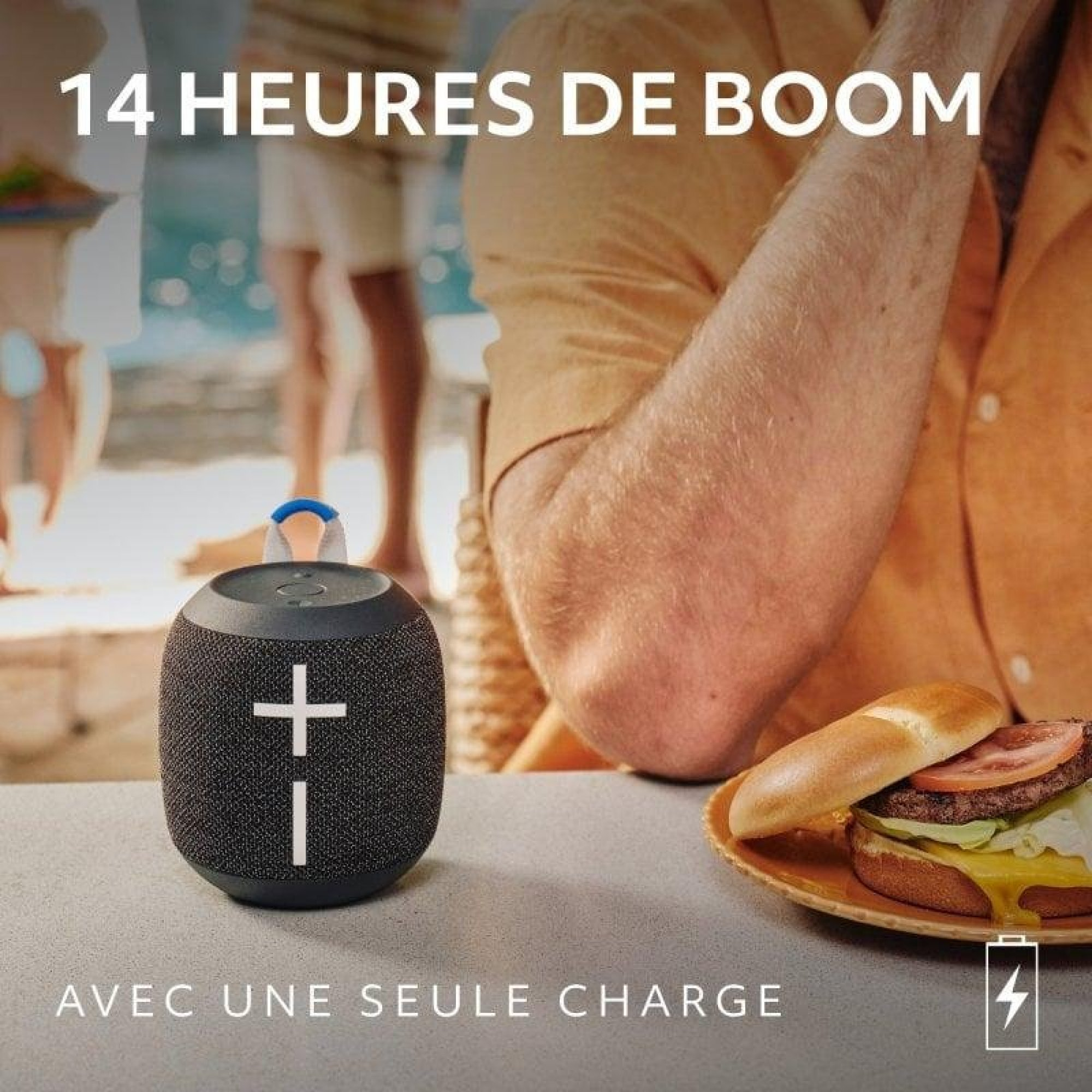Un altoparlante bluetooth portatile su un tavolo accanto a un hamburger. Sullo sfondo si vede una piscina.