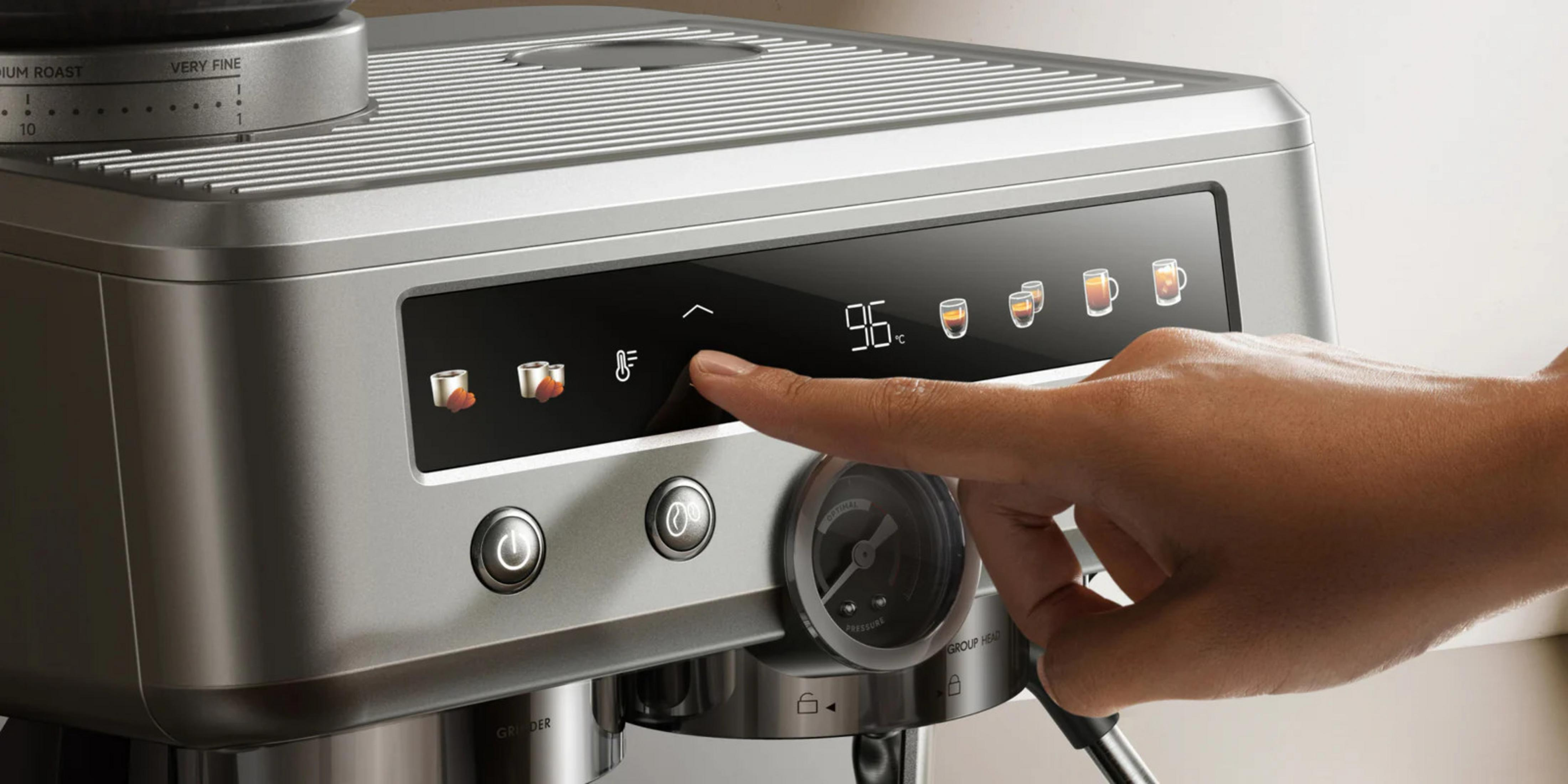 Una mano aziona il display touch di una moderna macchina da caffè espresso argentata con comandi digitali.