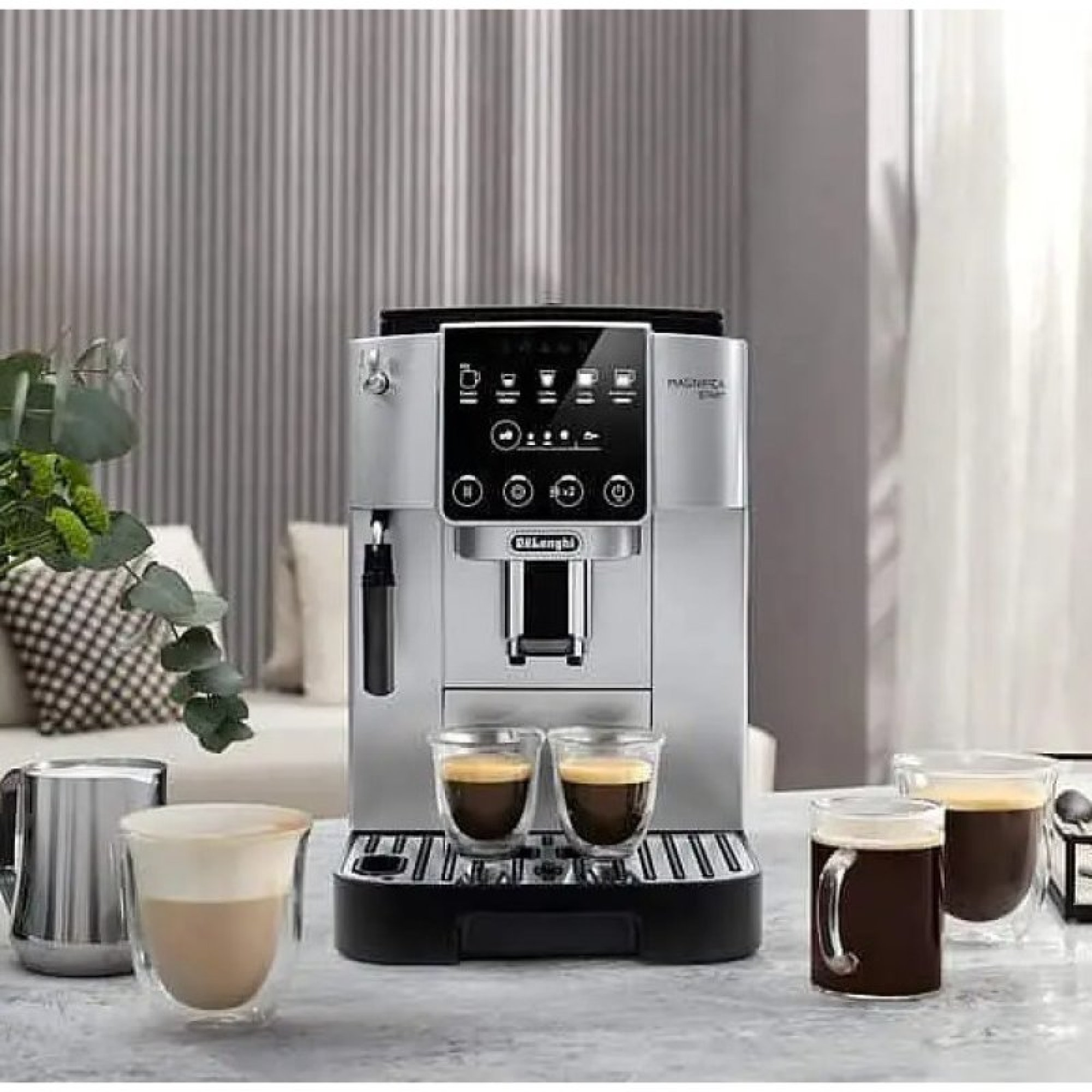 Una macchina da caffè espresso De'Longhi argentata su un bancone, con due tazzine di vetro e una lattiera.