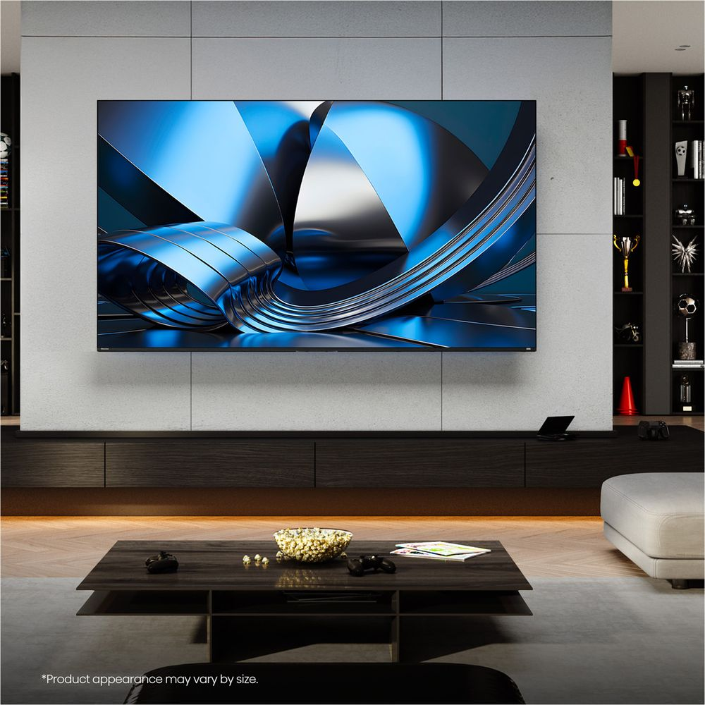 Soggiorno con grande TV a schermo piatto a parete, tavolino moderno con popcorn e libri, e scaffali sullo sfondo.