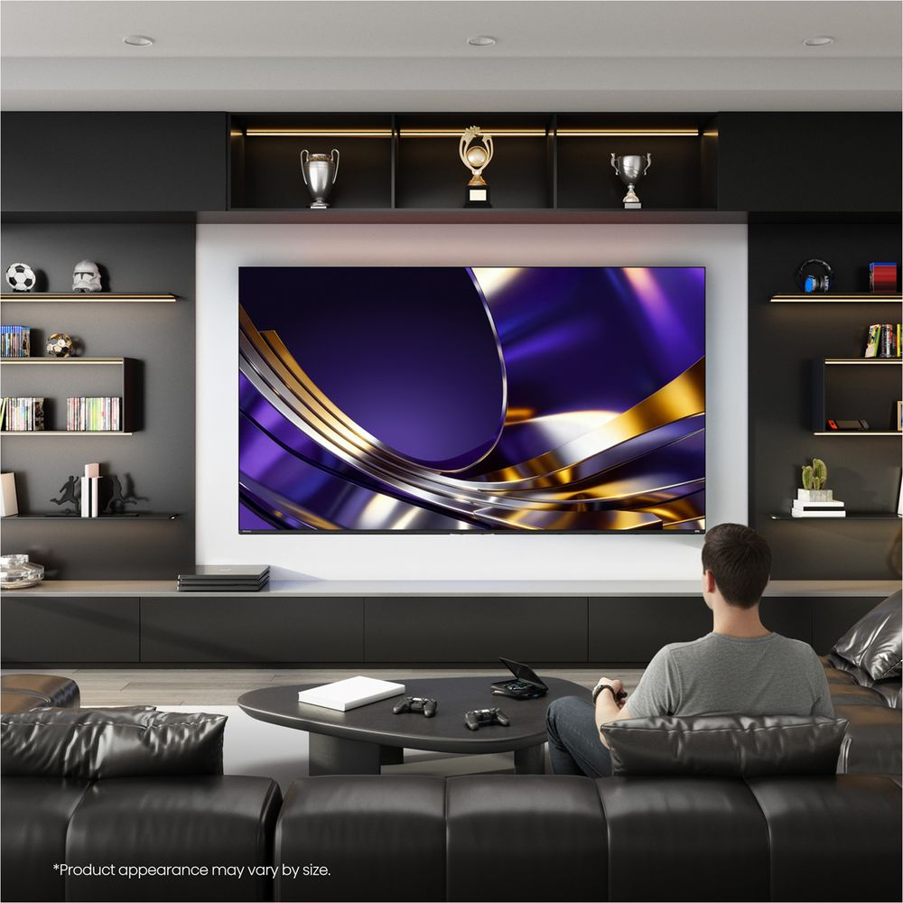 Un uomo siede su un divano in pelle nera in un soggiorno moderno, giocando a un videogioco su una grande TV.