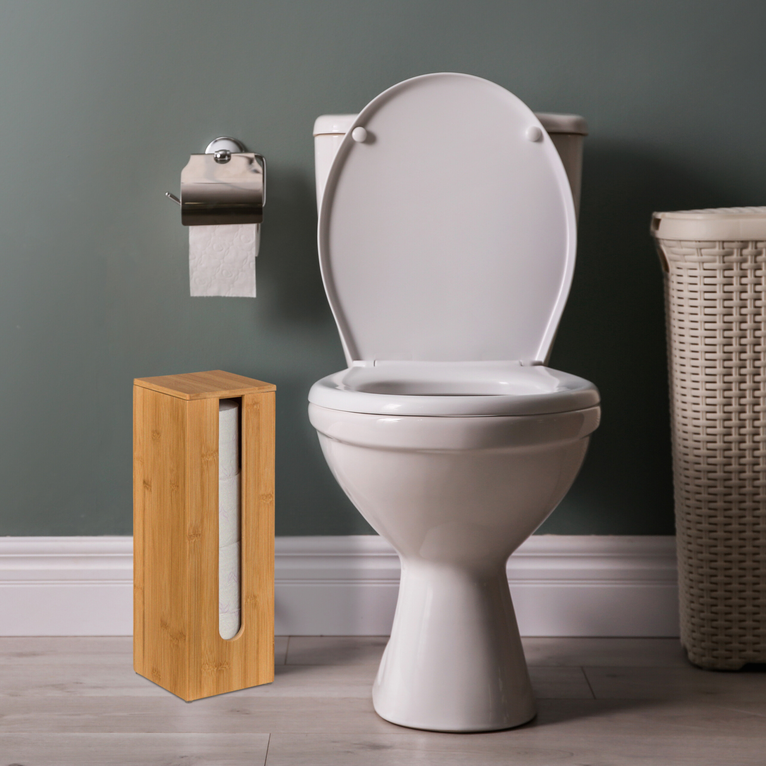 Eine weiße Toilette steht in einem Raum mit dunkelgrüner Wand. Links ist ein Toilettenpapierhalter aus Bambus.