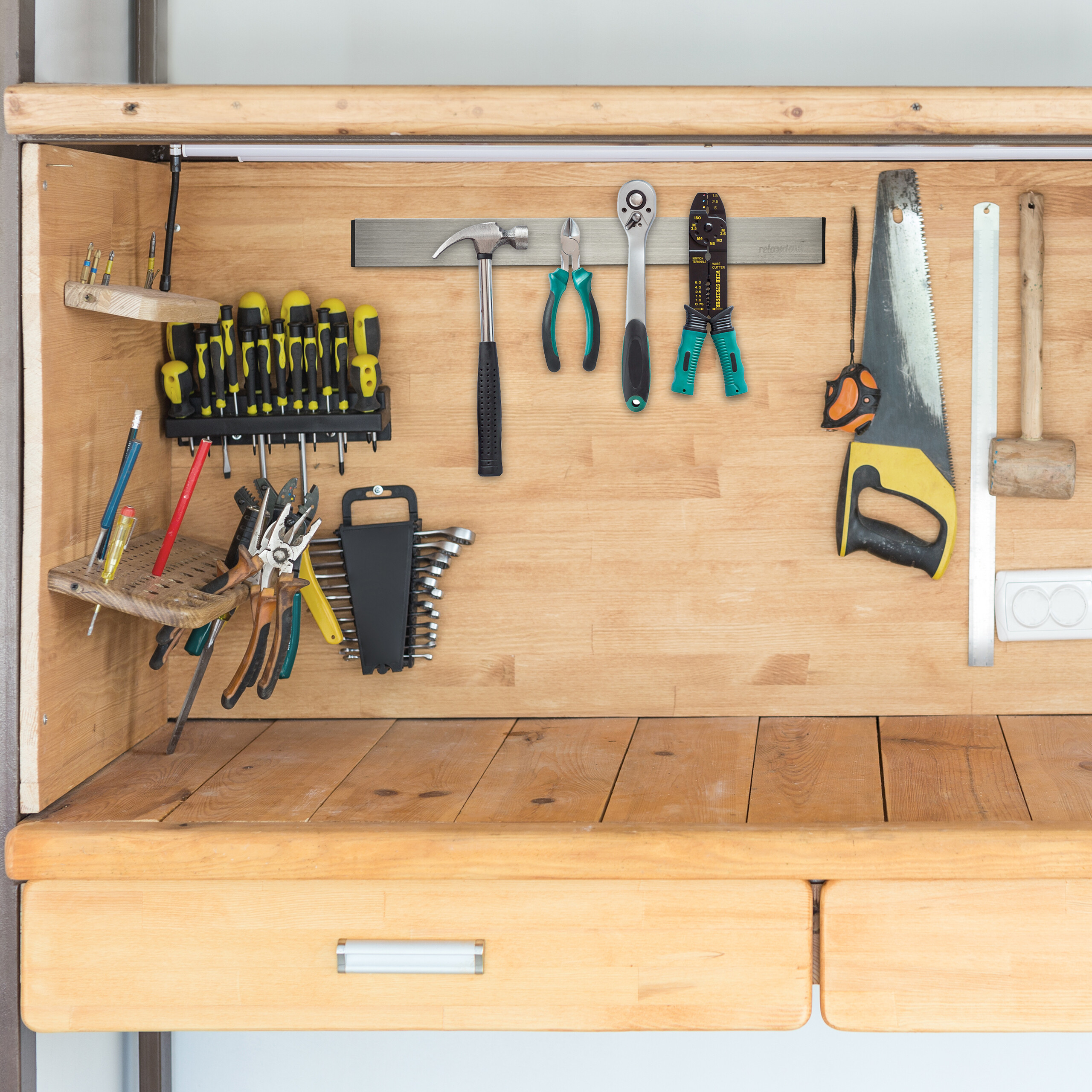 Eine Werkbank aus Holz mit ordentlich organisierten Werkzeugen an einer Magnetleiste und Regalen an einer Holzwand.