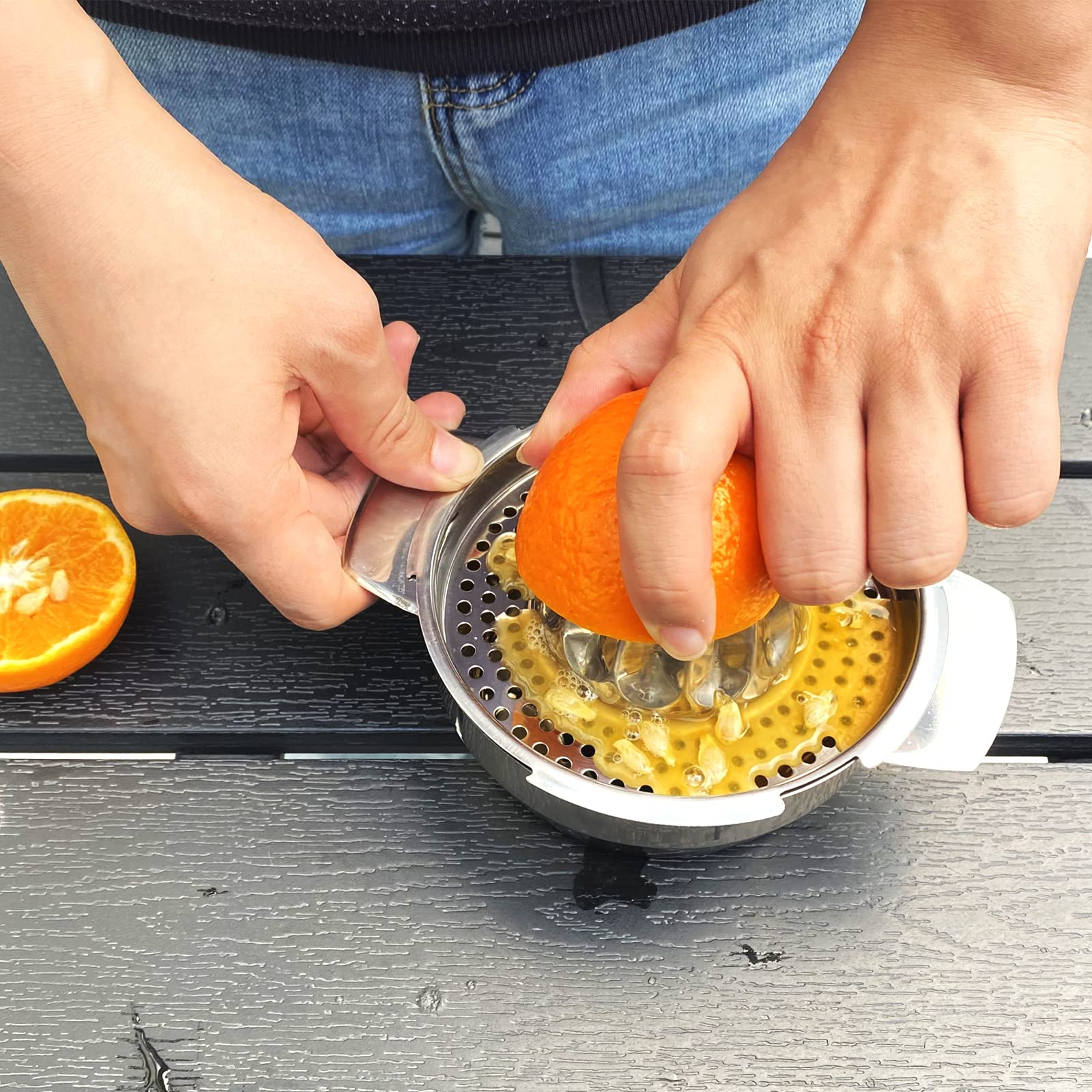 Person presst eine halbe Orange mit einer Hand auf einer Edelstahlpresse aus.