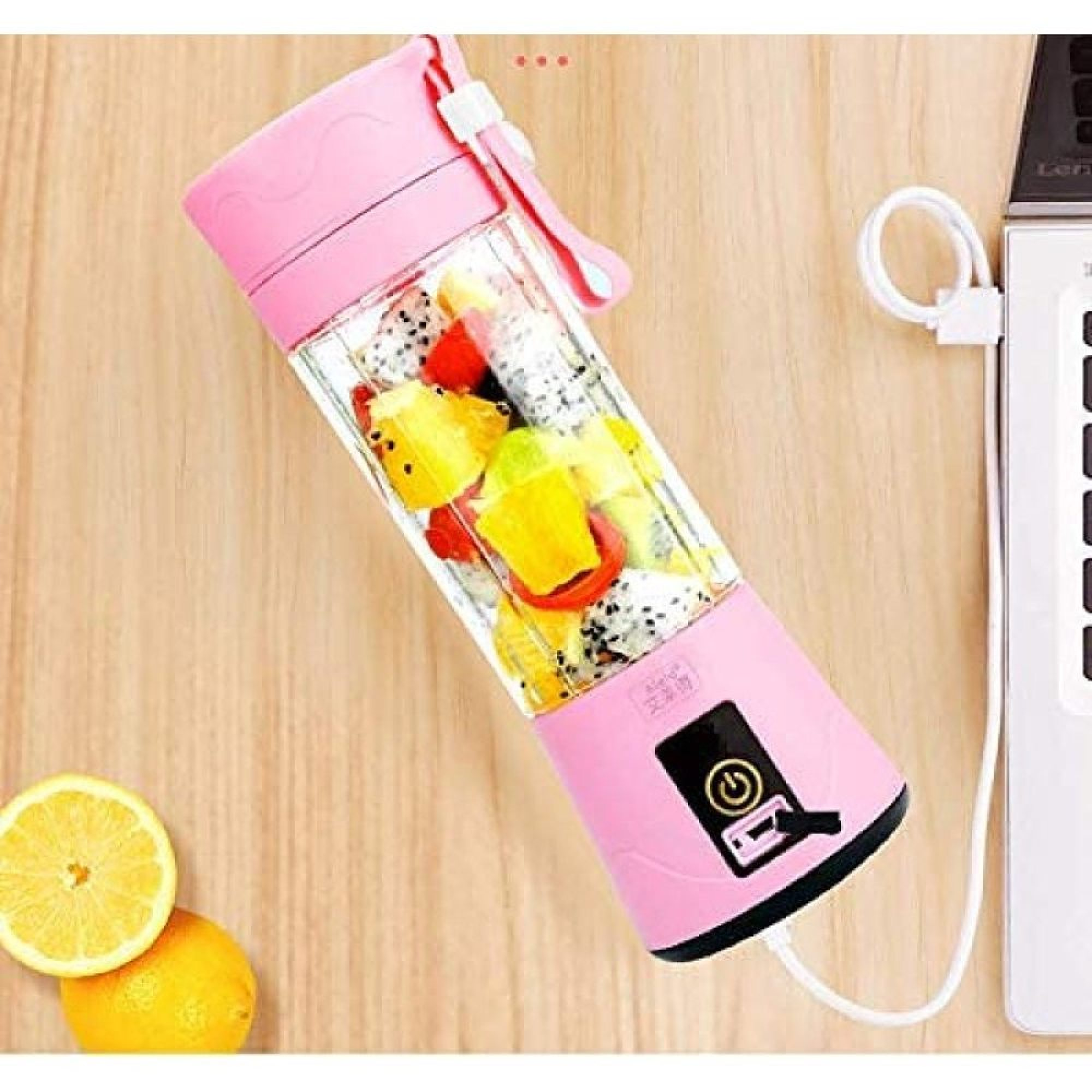Ein rosa tragbarer USB-Mixer mit Obststücken auf einem Holztisch neben einer aufgeschnittenen Zitrone.