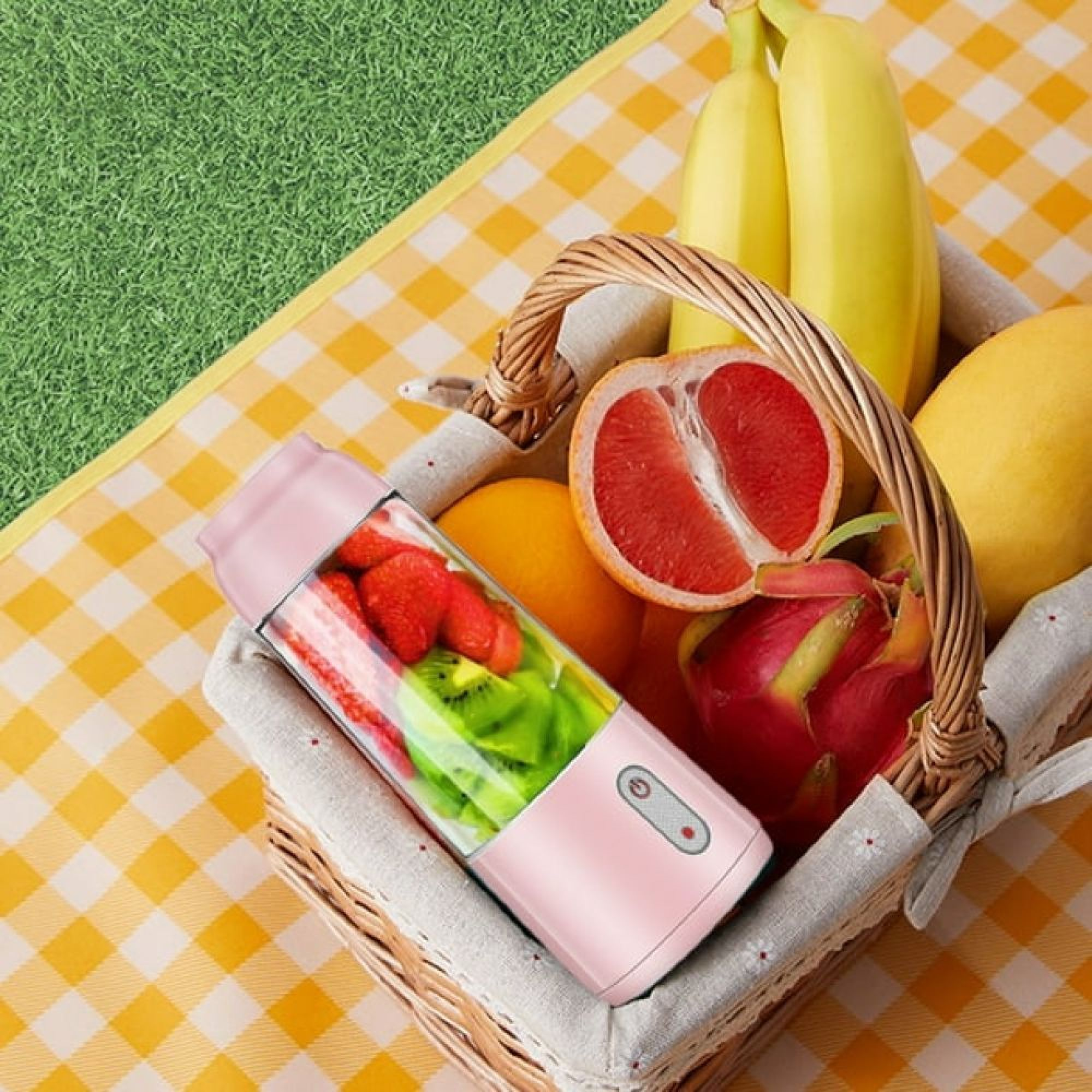 Ein Korb voller frischer Früchte und ein pinker Mixer auf einer gelb-weiß karierten Decke.