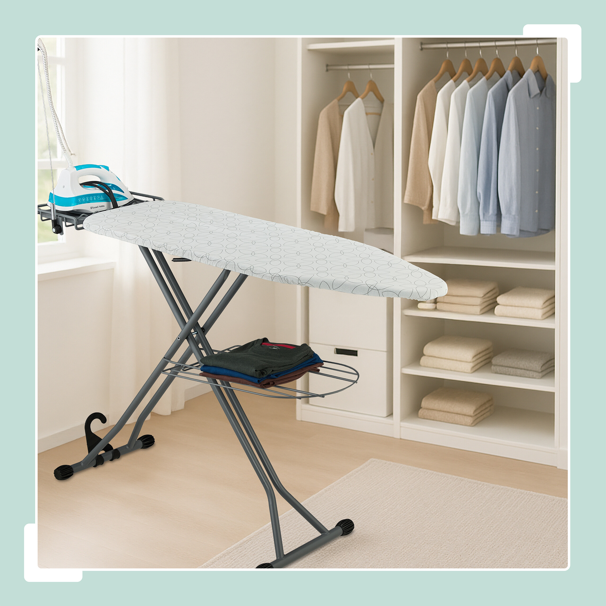 Ein Bügelbrett mit Eisen, gefaltete Kleidung auf einer Ablage und ein Kleiderschrank mit hängenden Hemden.