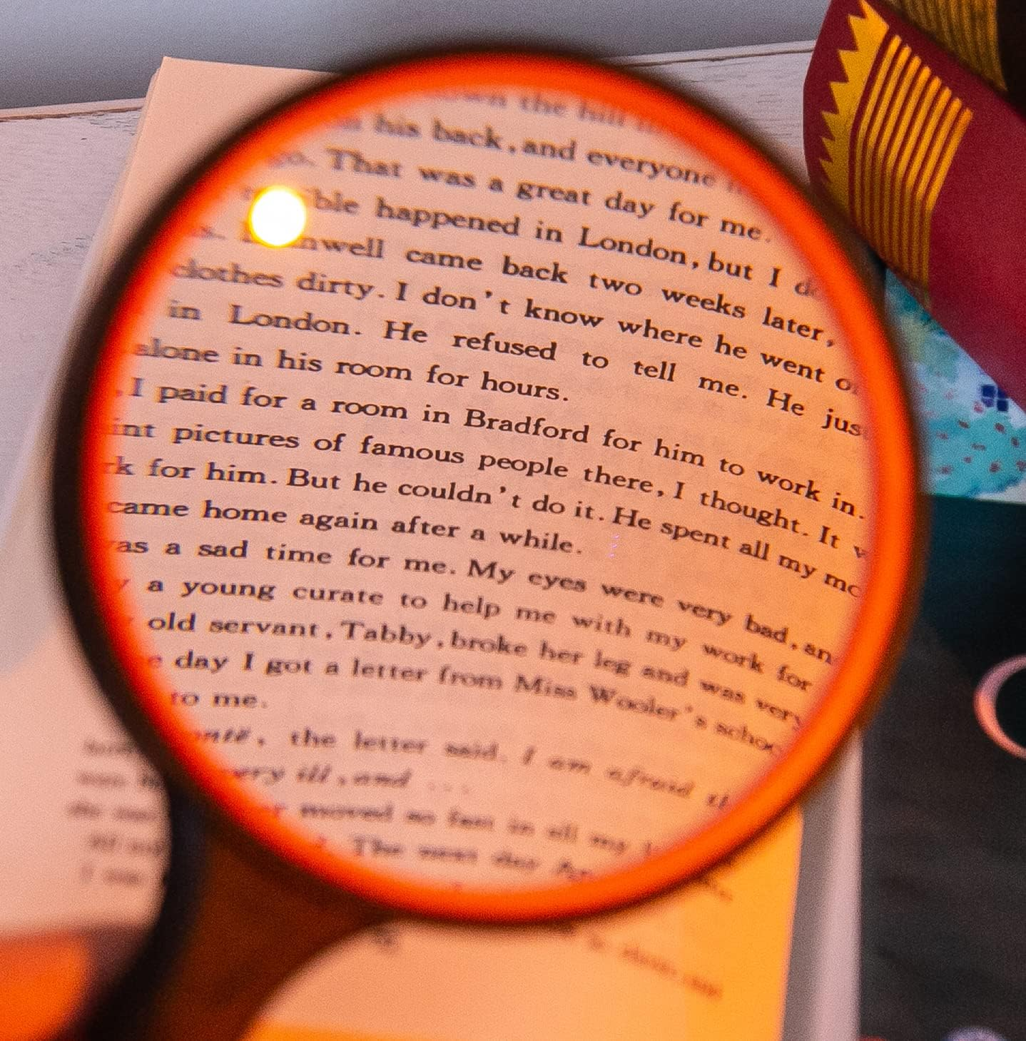 Eine Lupe schwebt über einer Buchseite und vergrößert Text mit hellem Glanz. Ein rot-gelber Schal ist sichtbar.