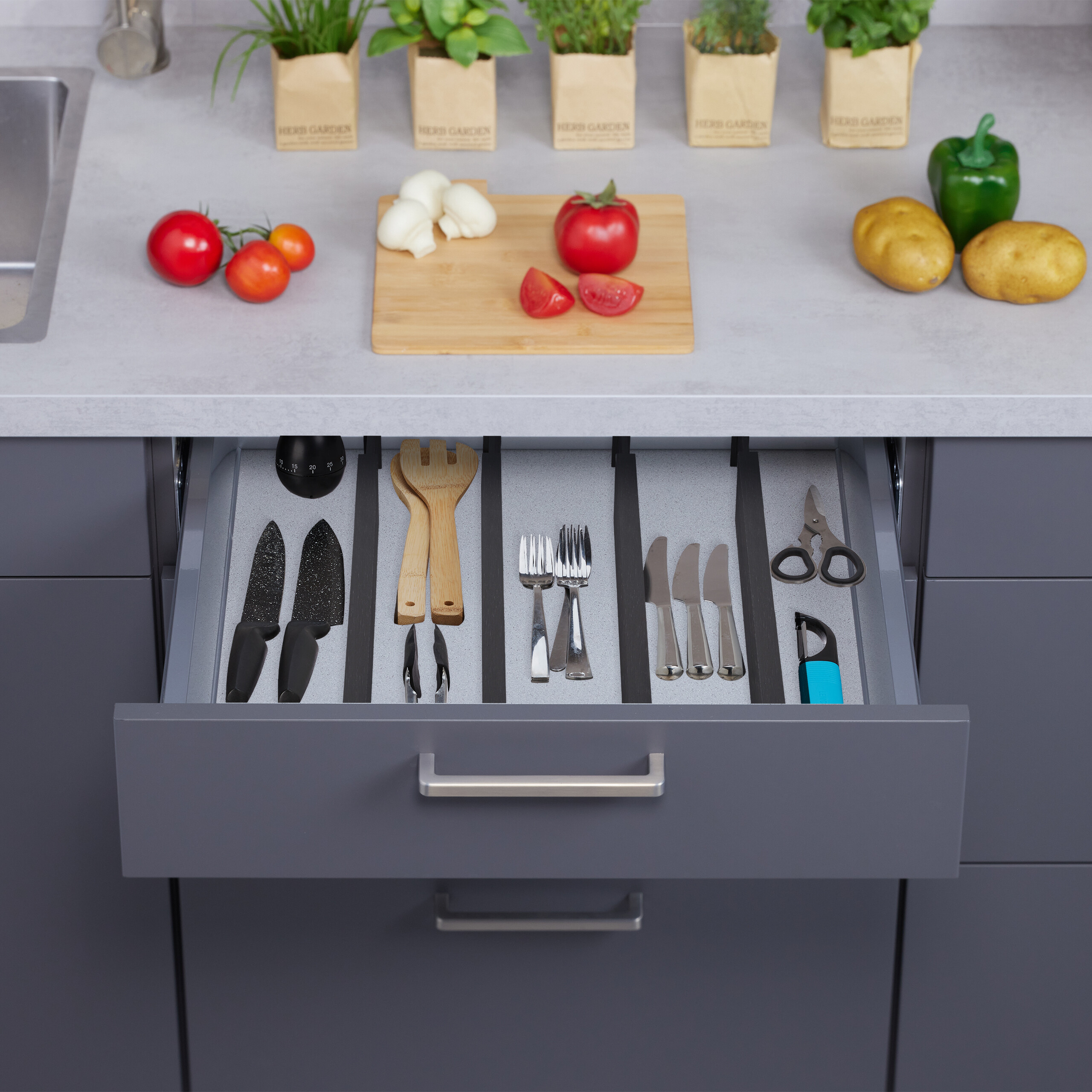 Eine geöffnete Küchenschublade mit organisiertem Besteck, Utensilien und Messern vor einer Küchentheke mit Lebensmitteln.