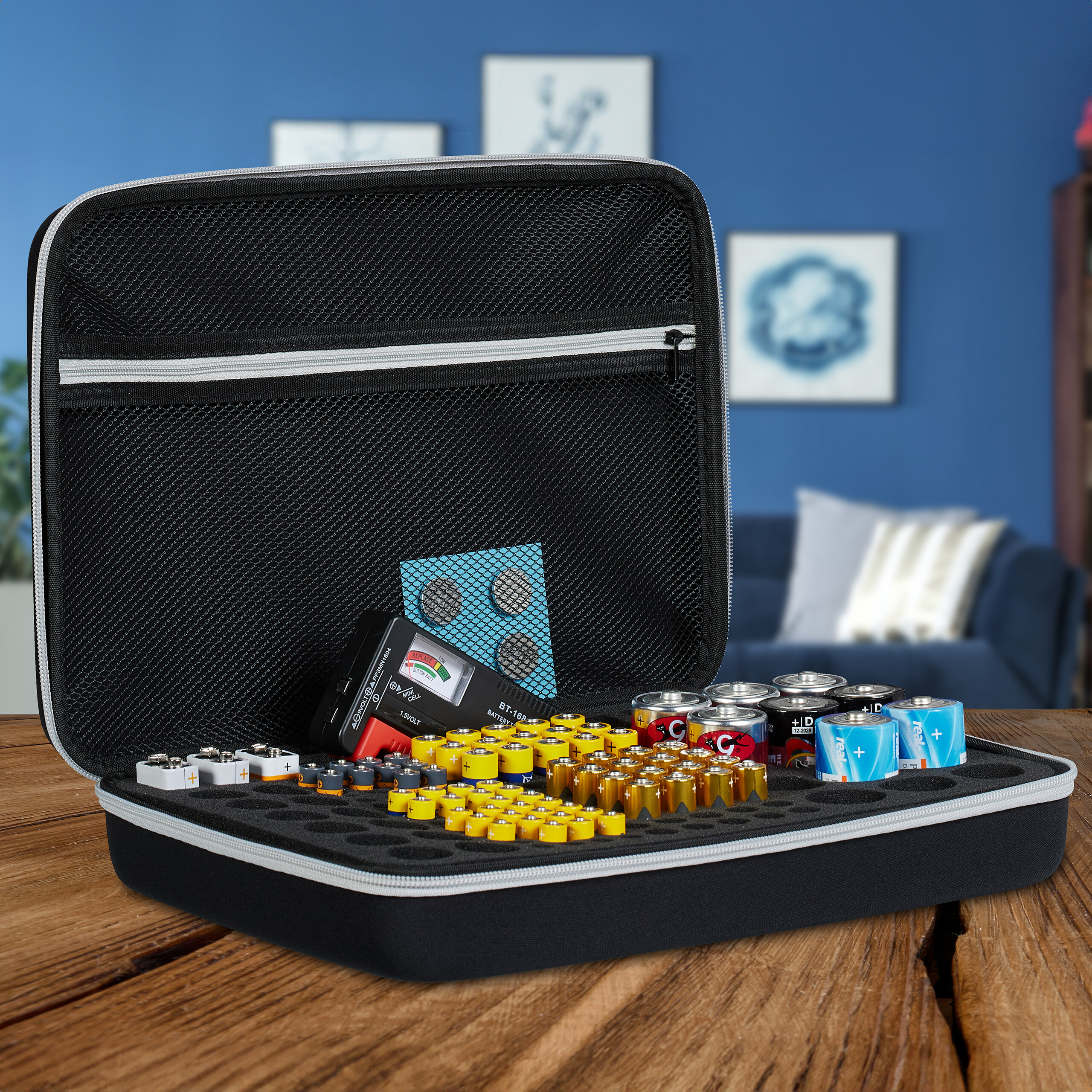 Eine offene schwarze Batterieaufbewahrungsbox gefüllt mit verschiedenen Batterien und einem Tester auf einem Holztisch.